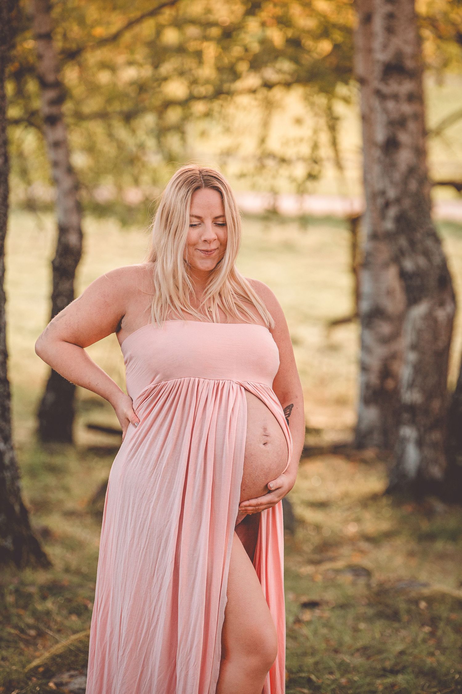 A maternity photoshoot in a forest setting with flowing pink fabric creating an ethereal autumn atmosphere.