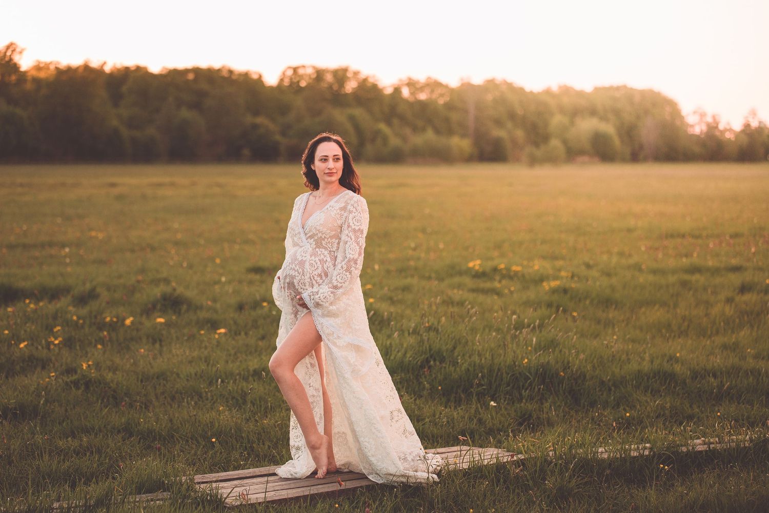 A flowing white lace dress catches the golden sunlight in a serene meadow at sunset.