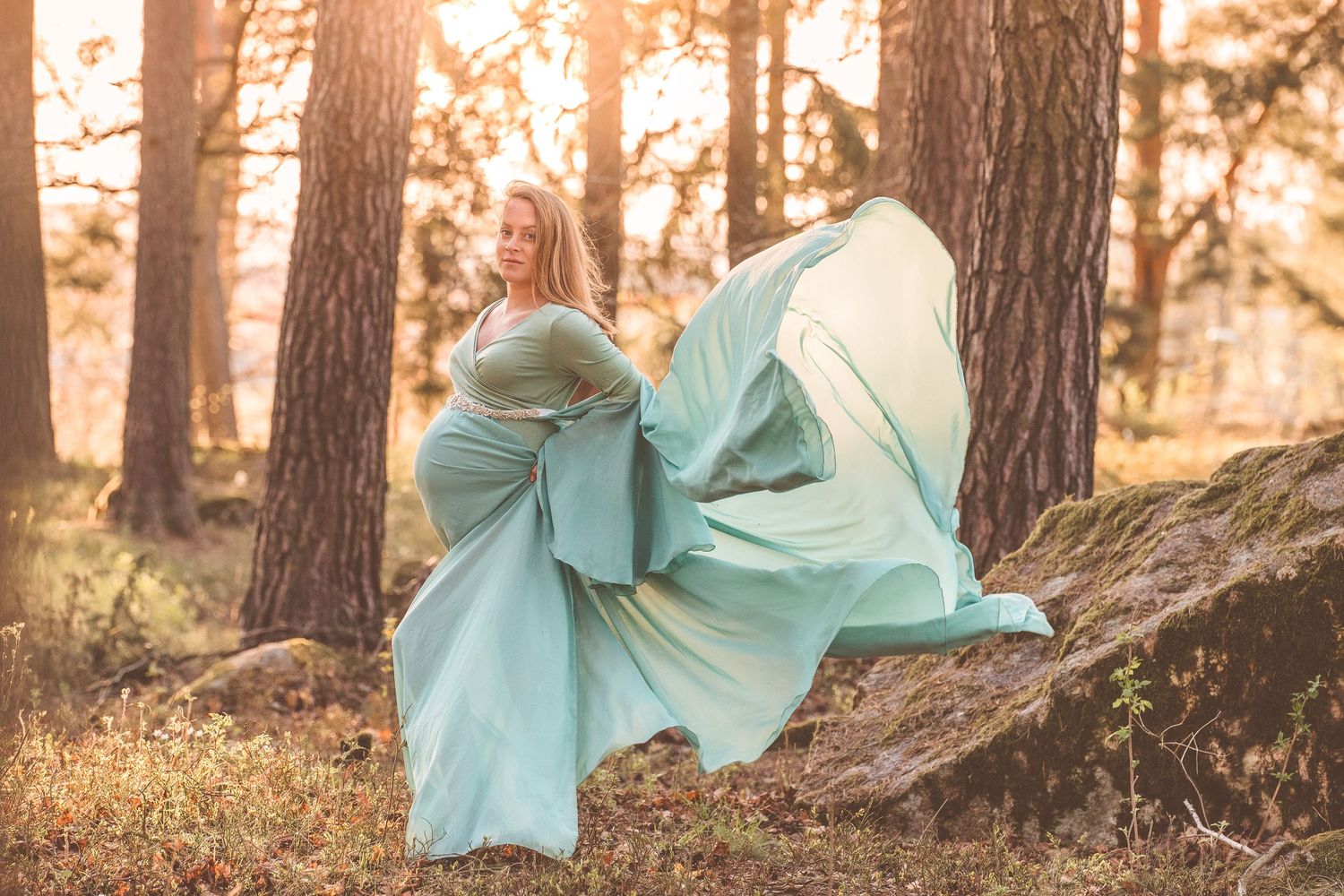 A person in a flowing turquoise dress twirls gracefully through a sunlit forest setting.