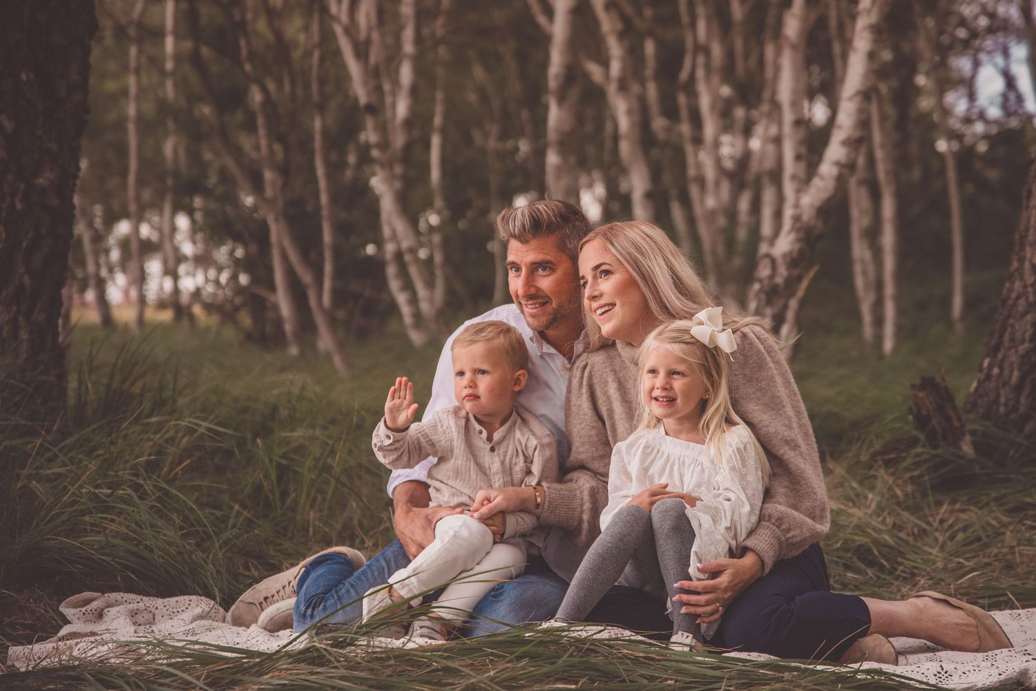 People relax together on tree logs in a peaceful woodland setting during sunset.