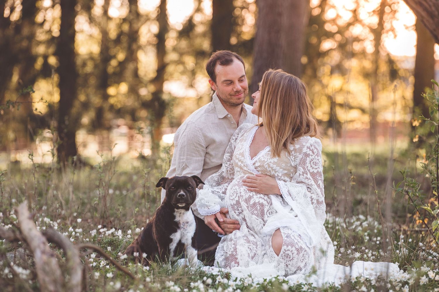 Couple embraces in a sunlit meadow filled with white wildflowers during golden hour.