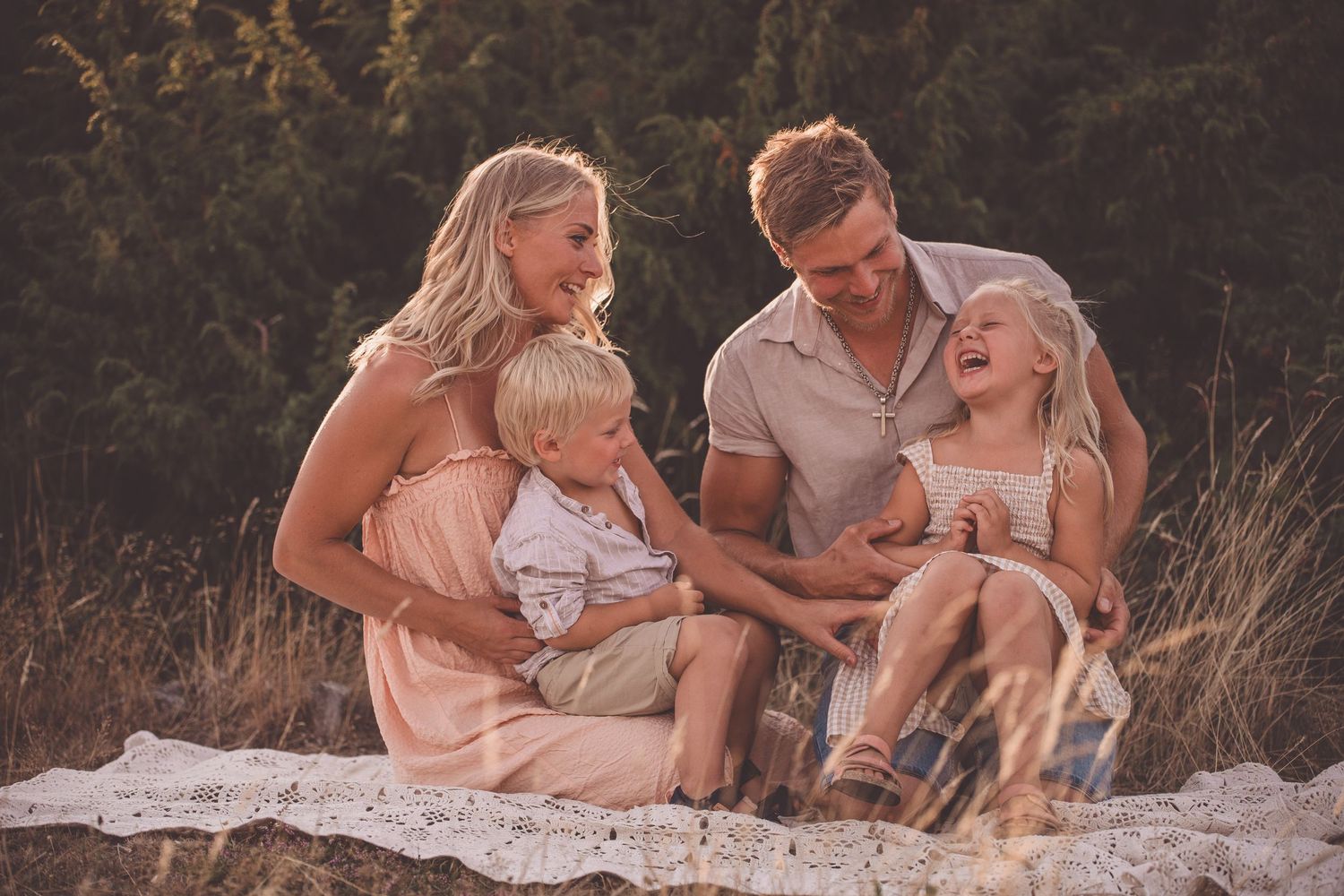 A family in light colored clothing sits together on a blanket during an outdoor golden hour photo session.