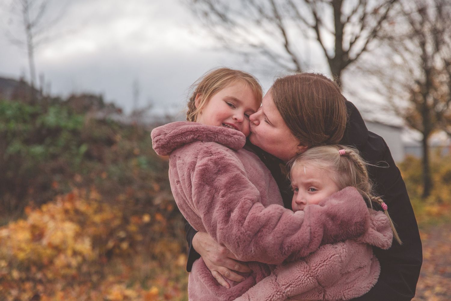 Two people share an embrace while wearing cozy pink jackets in an autumn setting.