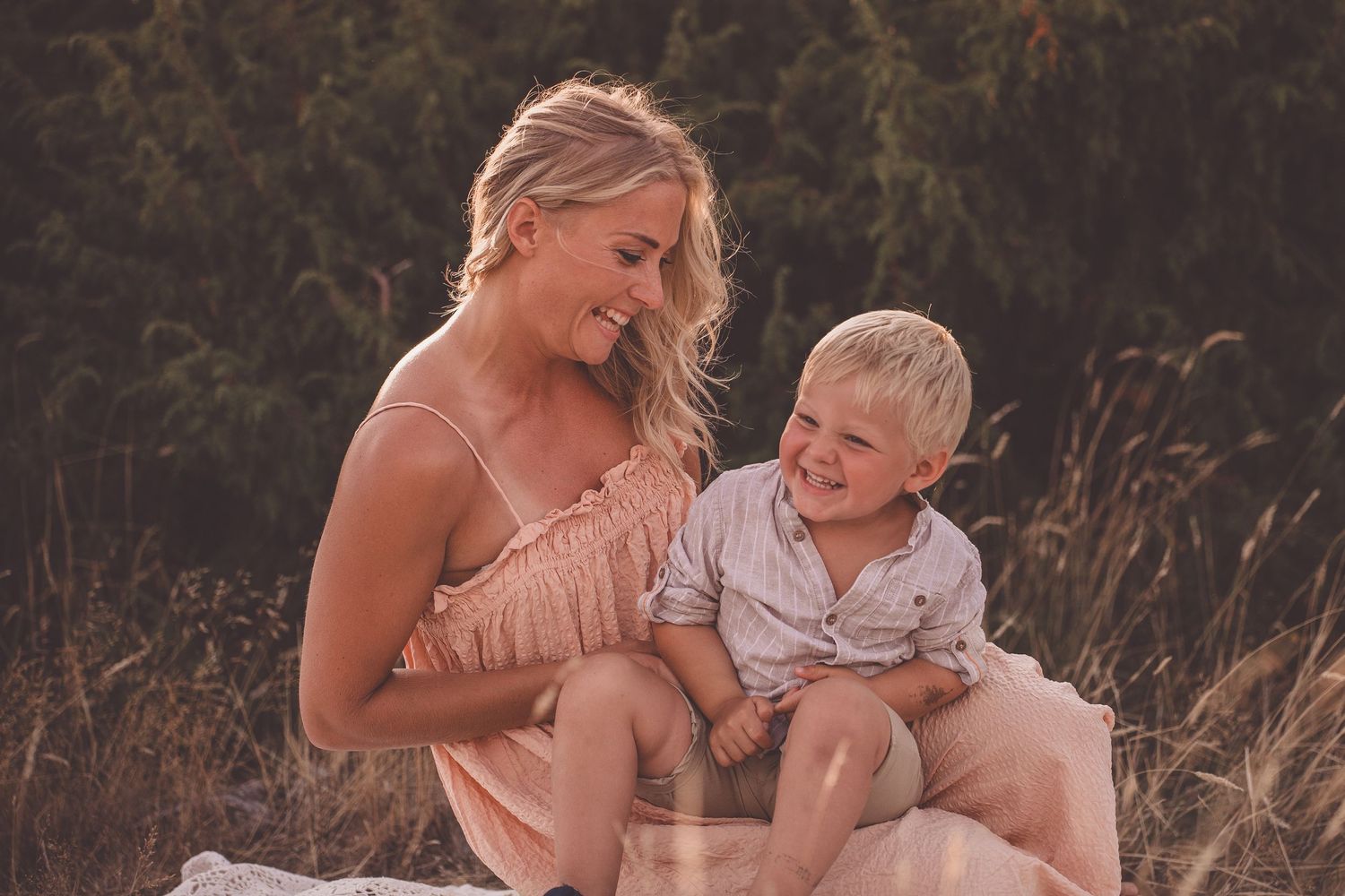 A parent and child share a joyful moment together while sitting in a field at sunset.
