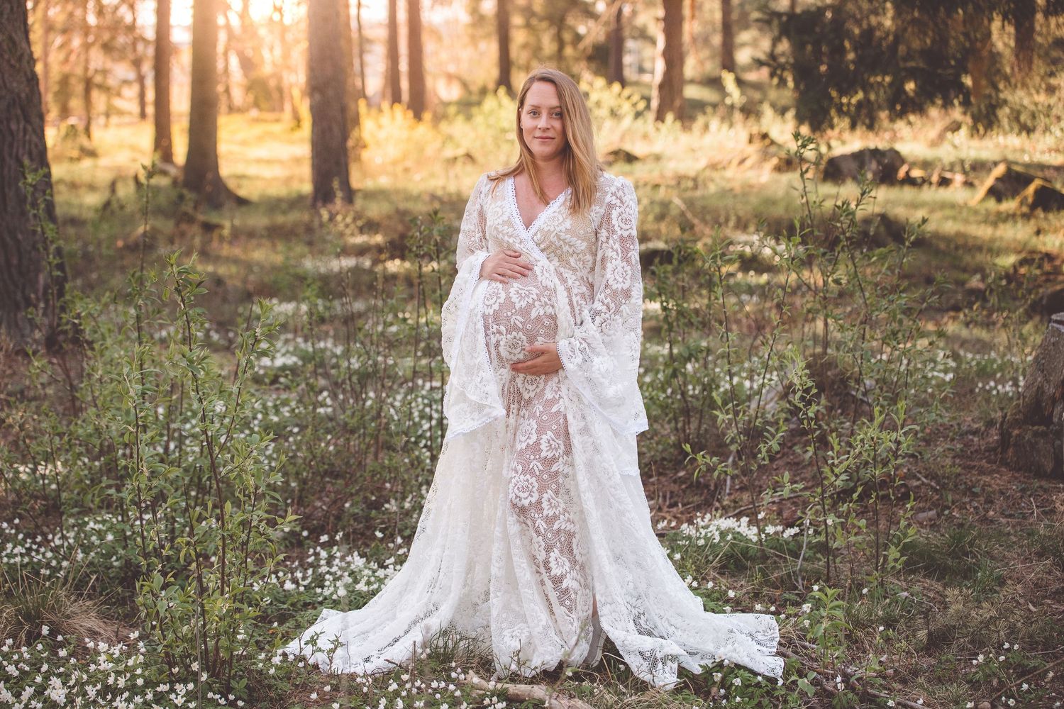 A romantic bridal portrait in a sun-dappled forest with white lace dress and flowing veil among wildflowers.
