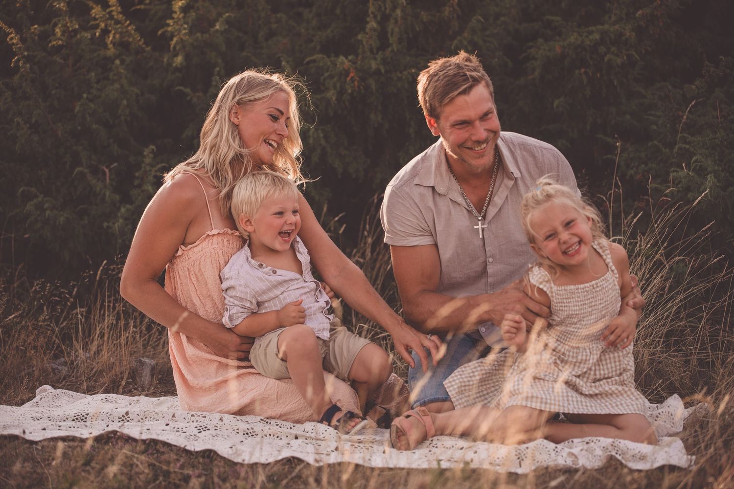 A family sits together on a blanket outdoors during golden hour, enjoying a peaceful moment in nature.