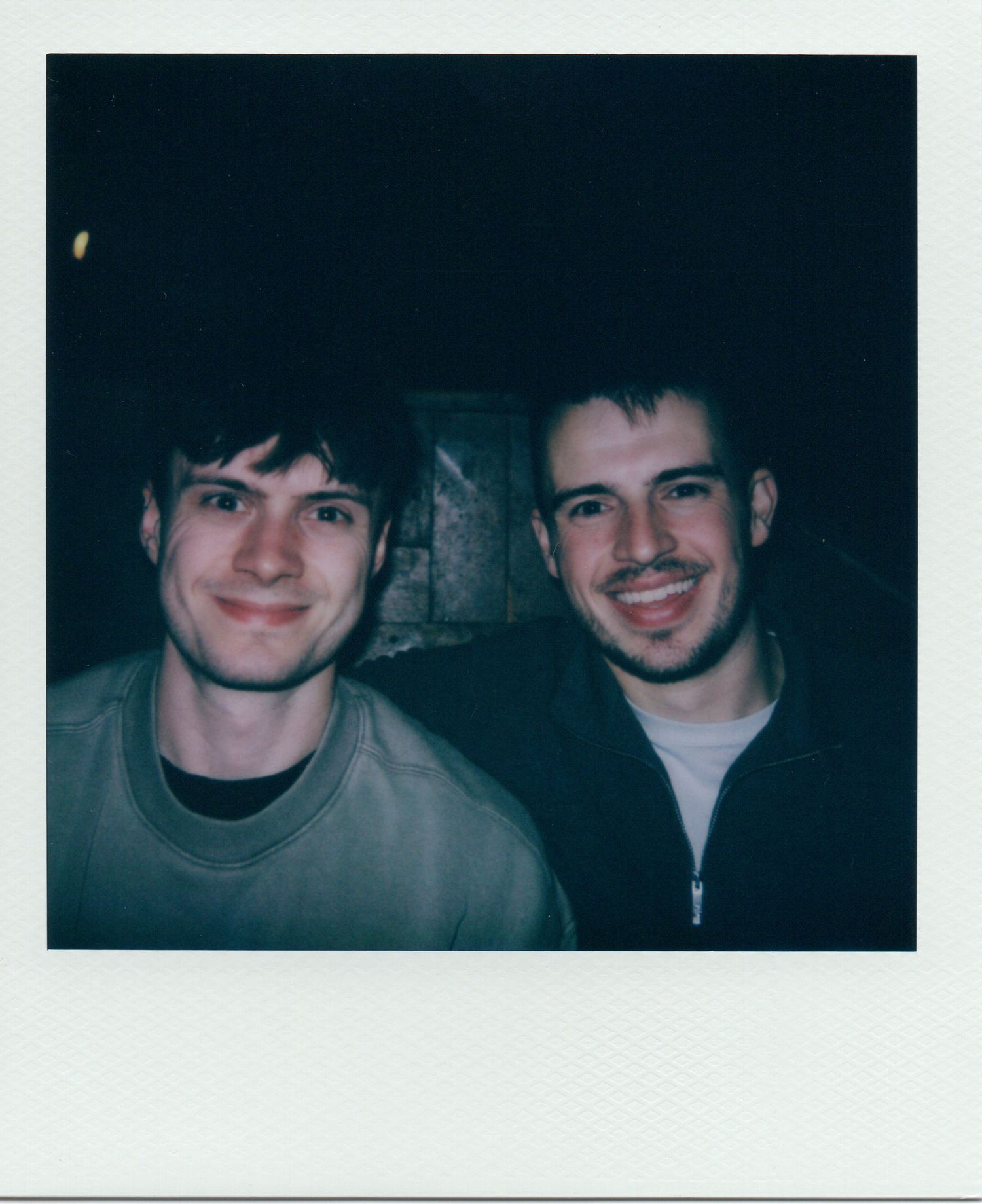 Polaroid portrait of two young men smiling together against a dark background at night.