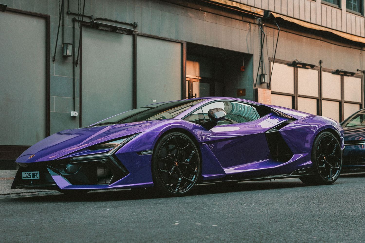 A stunning purple Lamborghini supercar parked on a city street, showcasing its aggressive aerodynamic design and black alloy wheels.