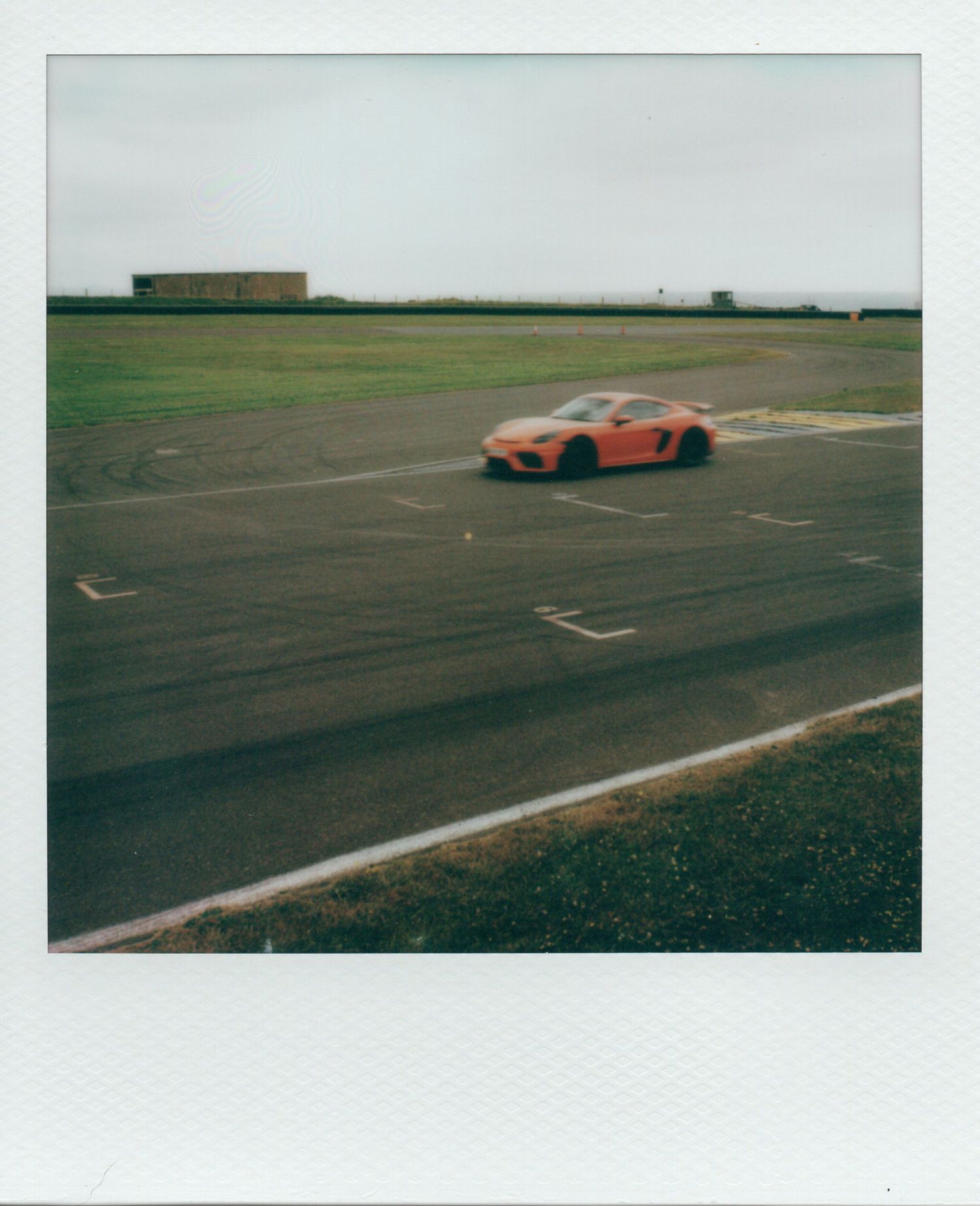 Orange Porsche sports car speeding on a race track with green fields in the background.