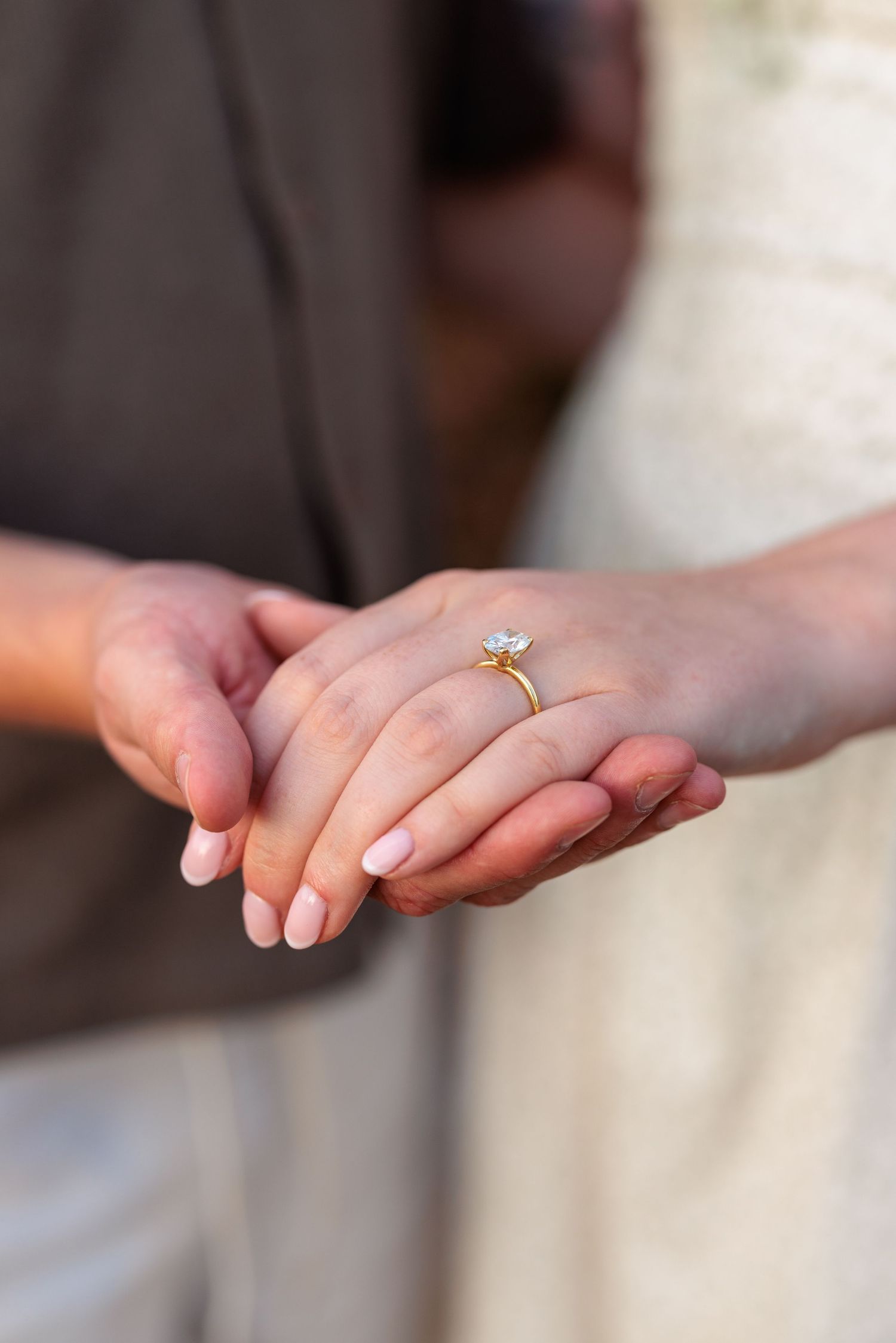 Close-up of a couple holding hands, showcasing a gold diamond engagement ring on the bride's finger.