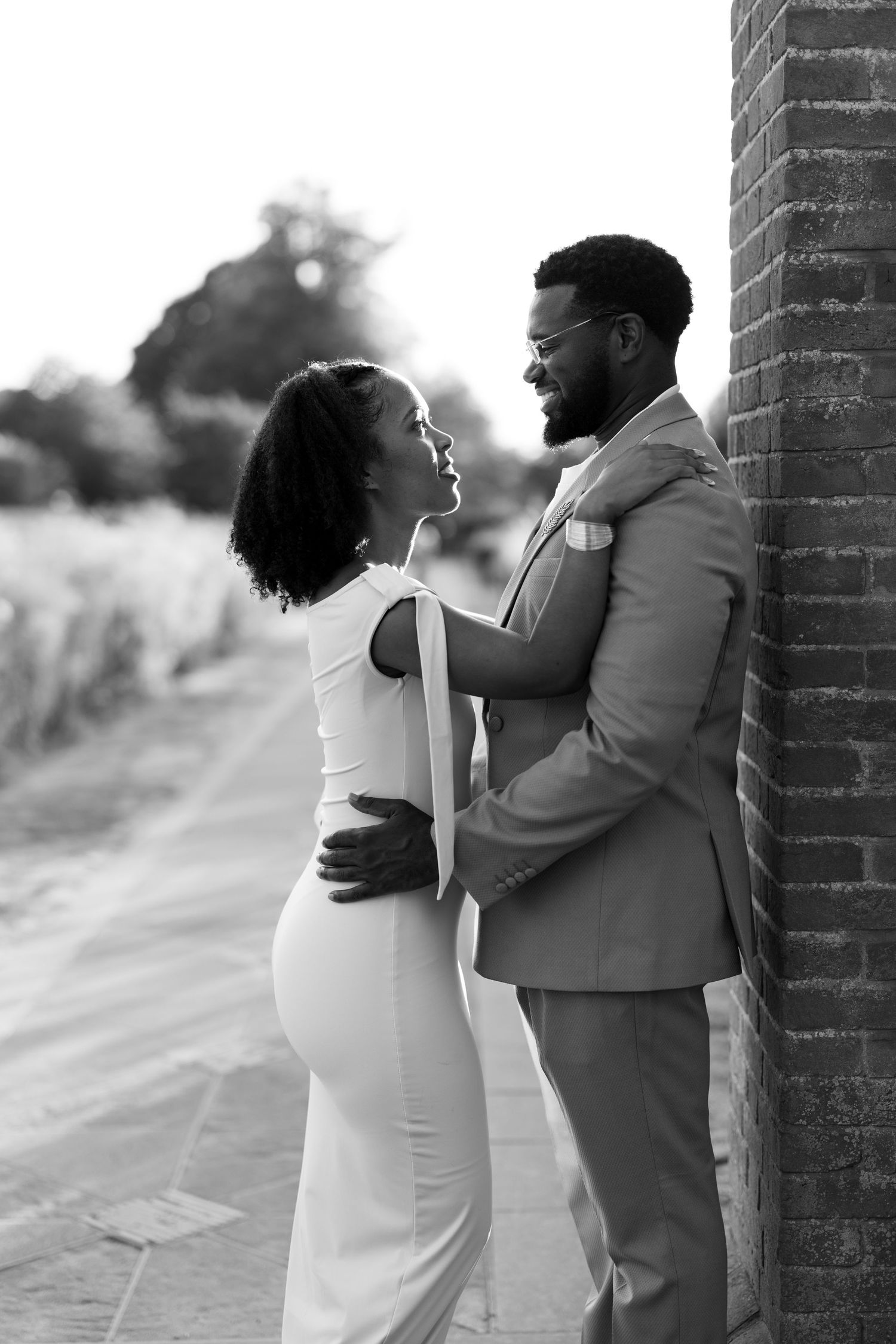 Black and white photo of a couple in wedding attire embracing and smiling at each other outdoors.