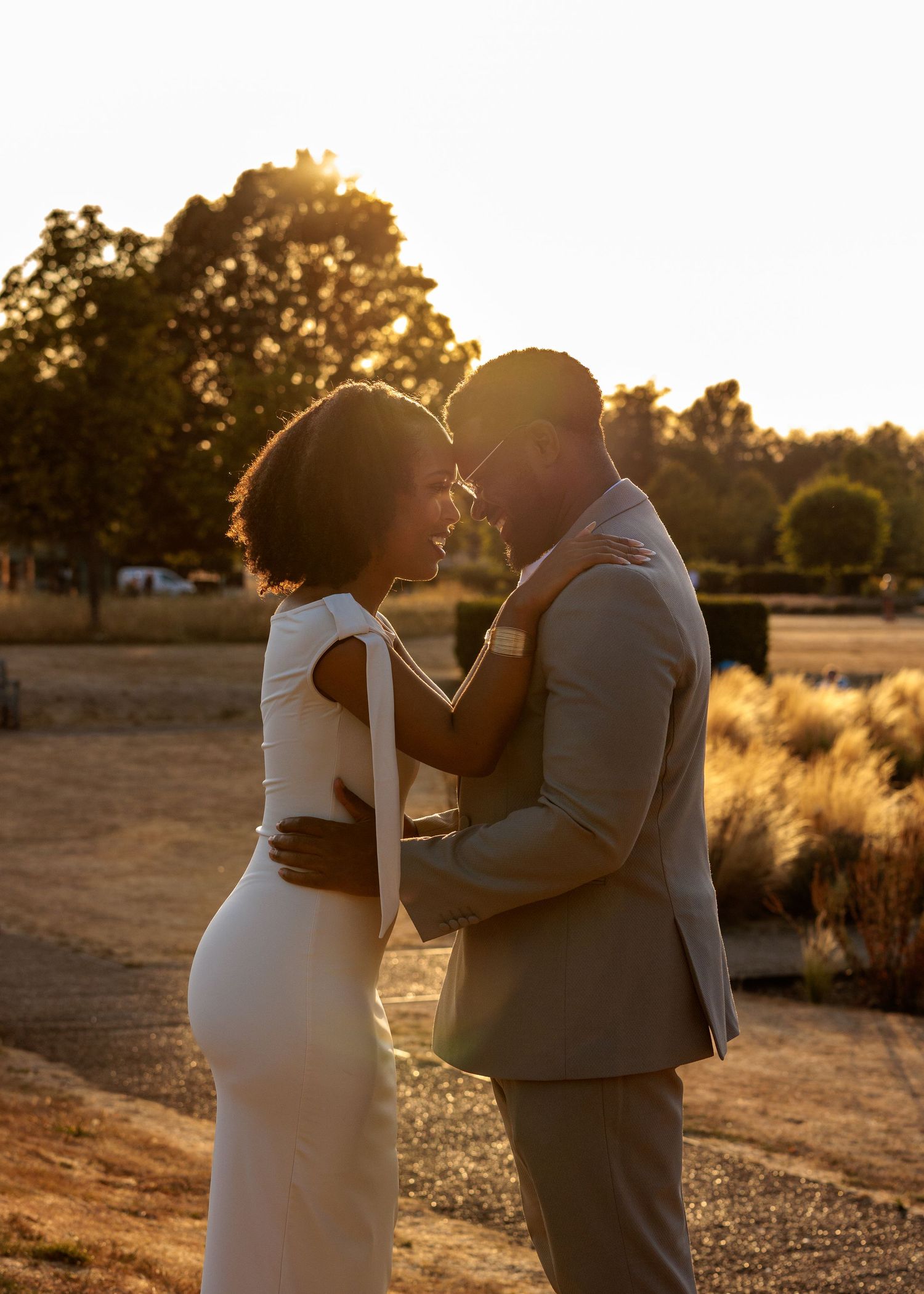 Couple in wedding attire sharing a romantic moment at golden hour sunset outdoors.
