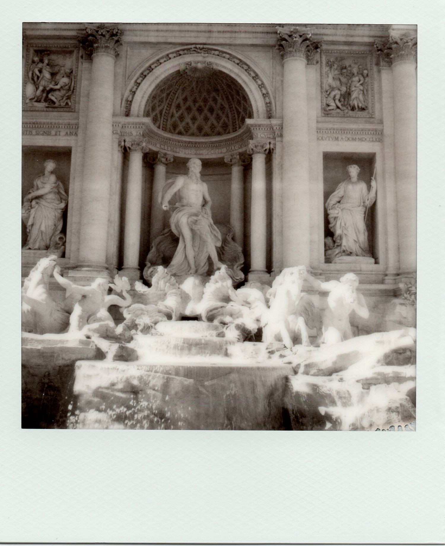 Black and white Polaroid of the Trevi Fountain in Rome, featuring Neptune statue and baroque architecture.