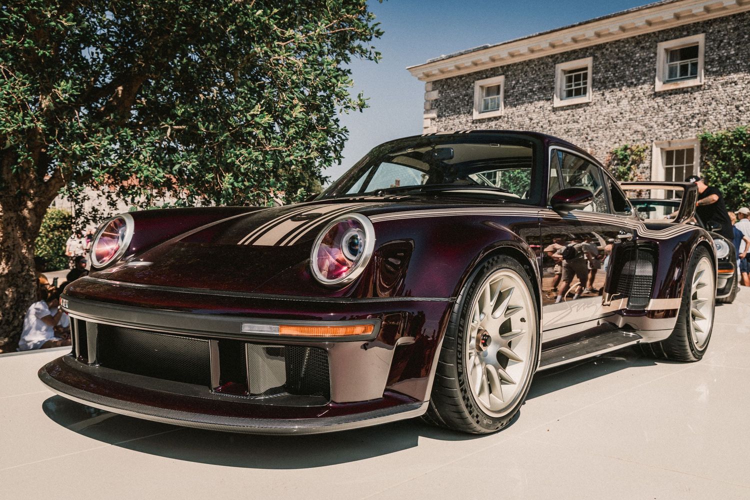 Custom dark purple Porsche 930 Turbo widebody restomod on display at an outdoor car show.