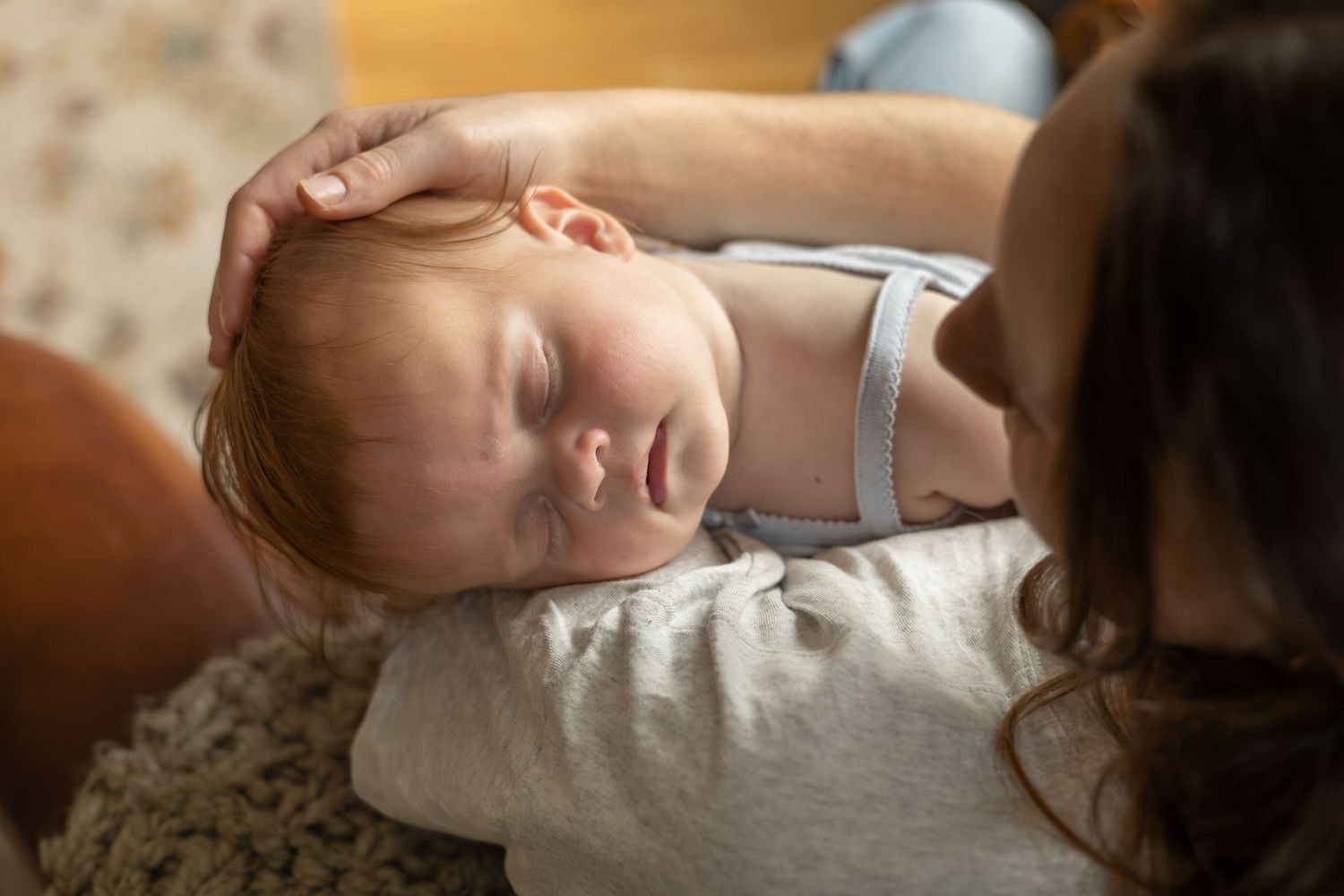 A baby falls asleep on her mom's shoulder in their living room.