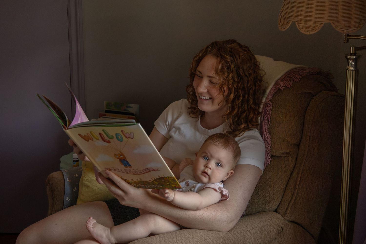 A mom cuddles with her baby in a chair in the nursery while reading her a story.