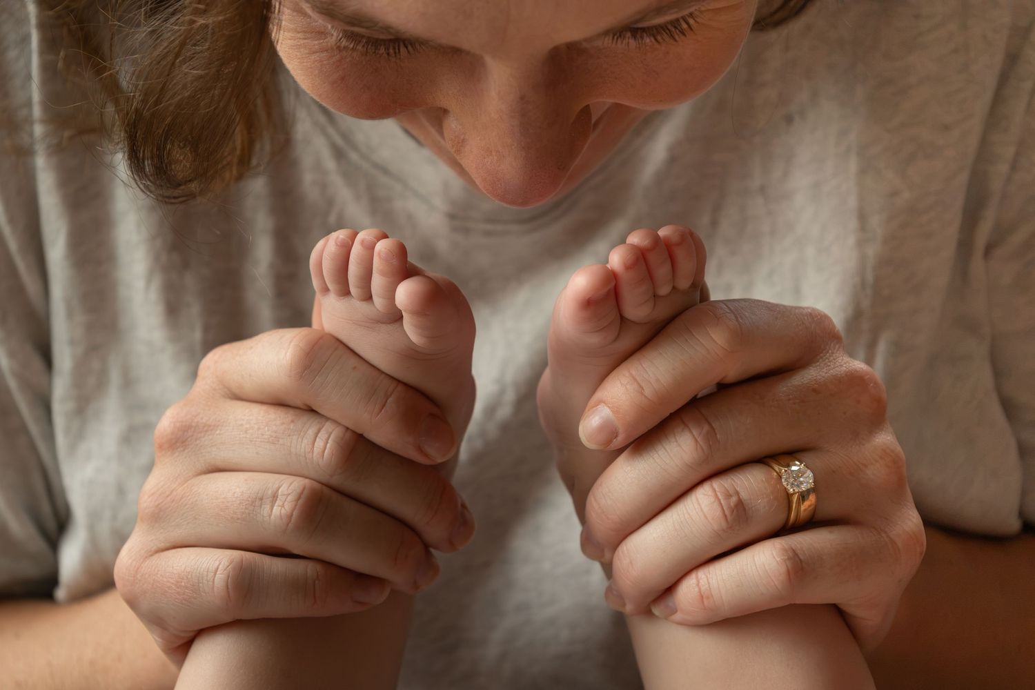A mom smiles down at a baby in her lap while she holds the baby's feet together up towards her face.