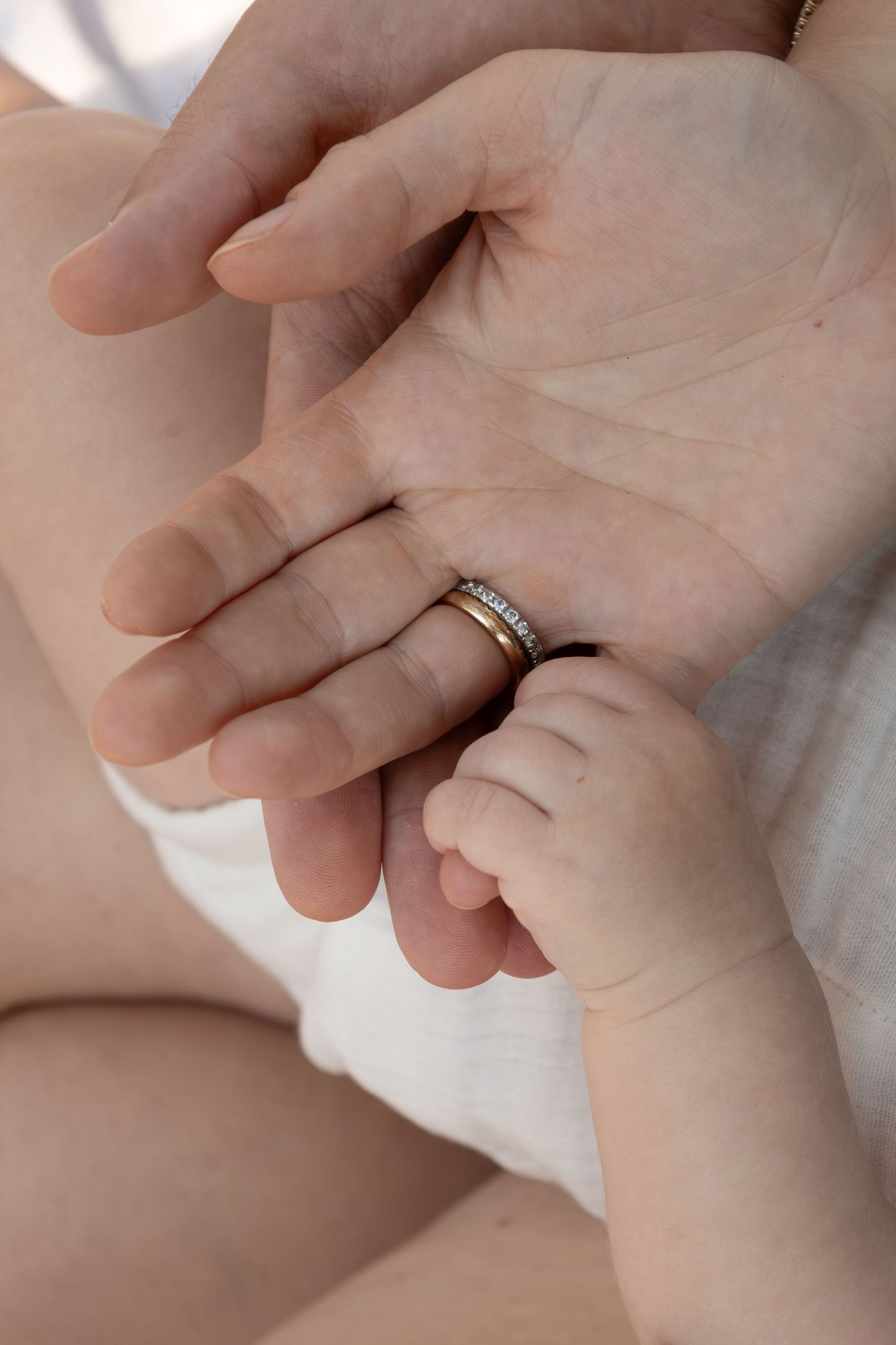 A baby holds onto their mom's pinky finger while the dad's hand rests beneath theirs.