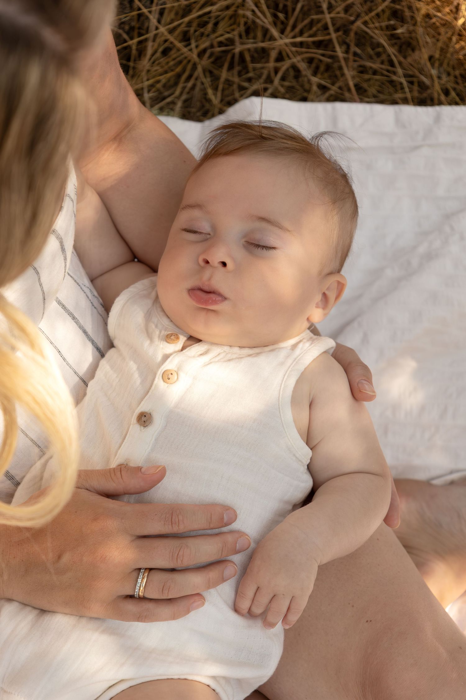 A baby sleeps in his moms lap as she rests her hand on his belly.