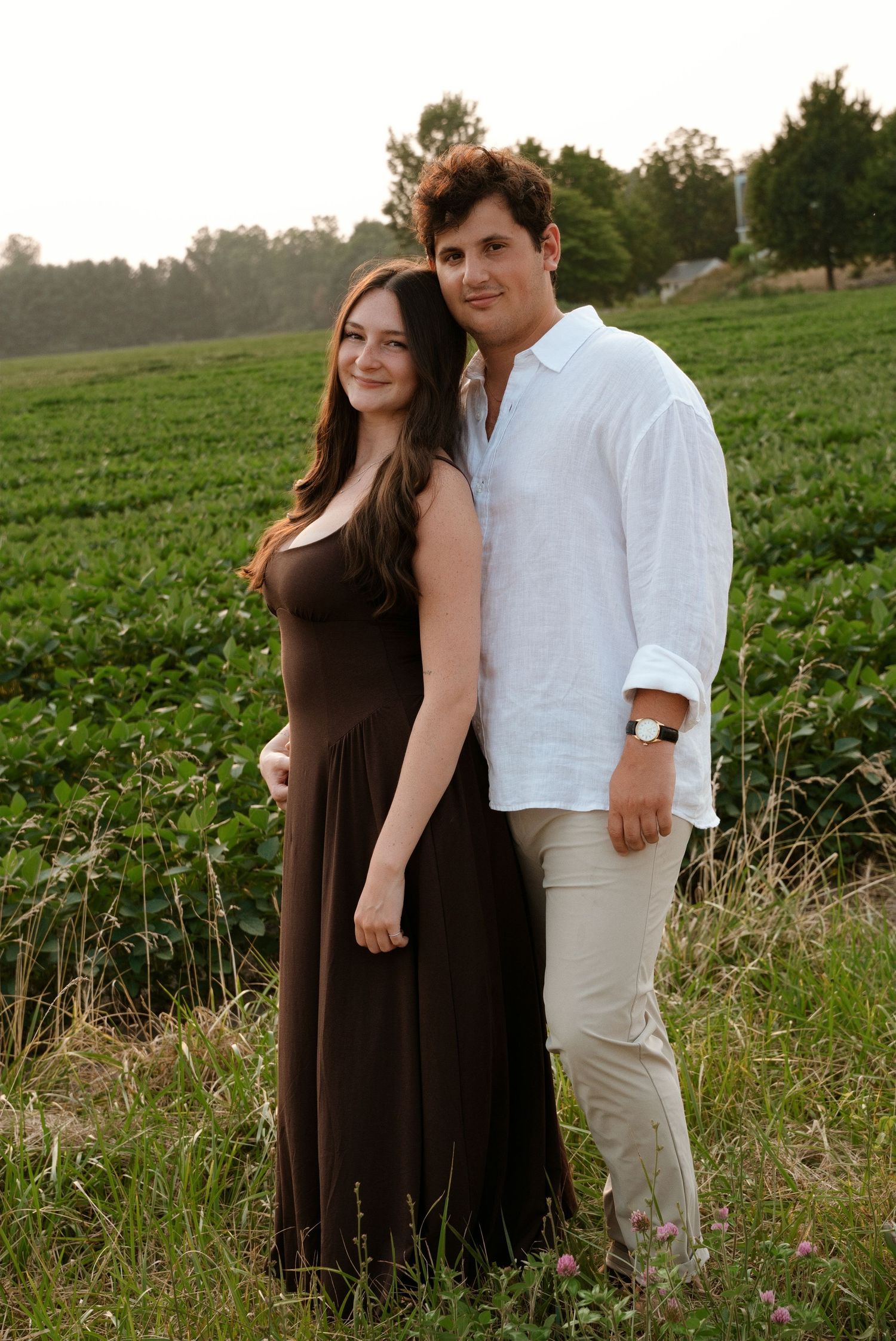 Smiling couple posing together in a green countryside field during warm golden hour light.