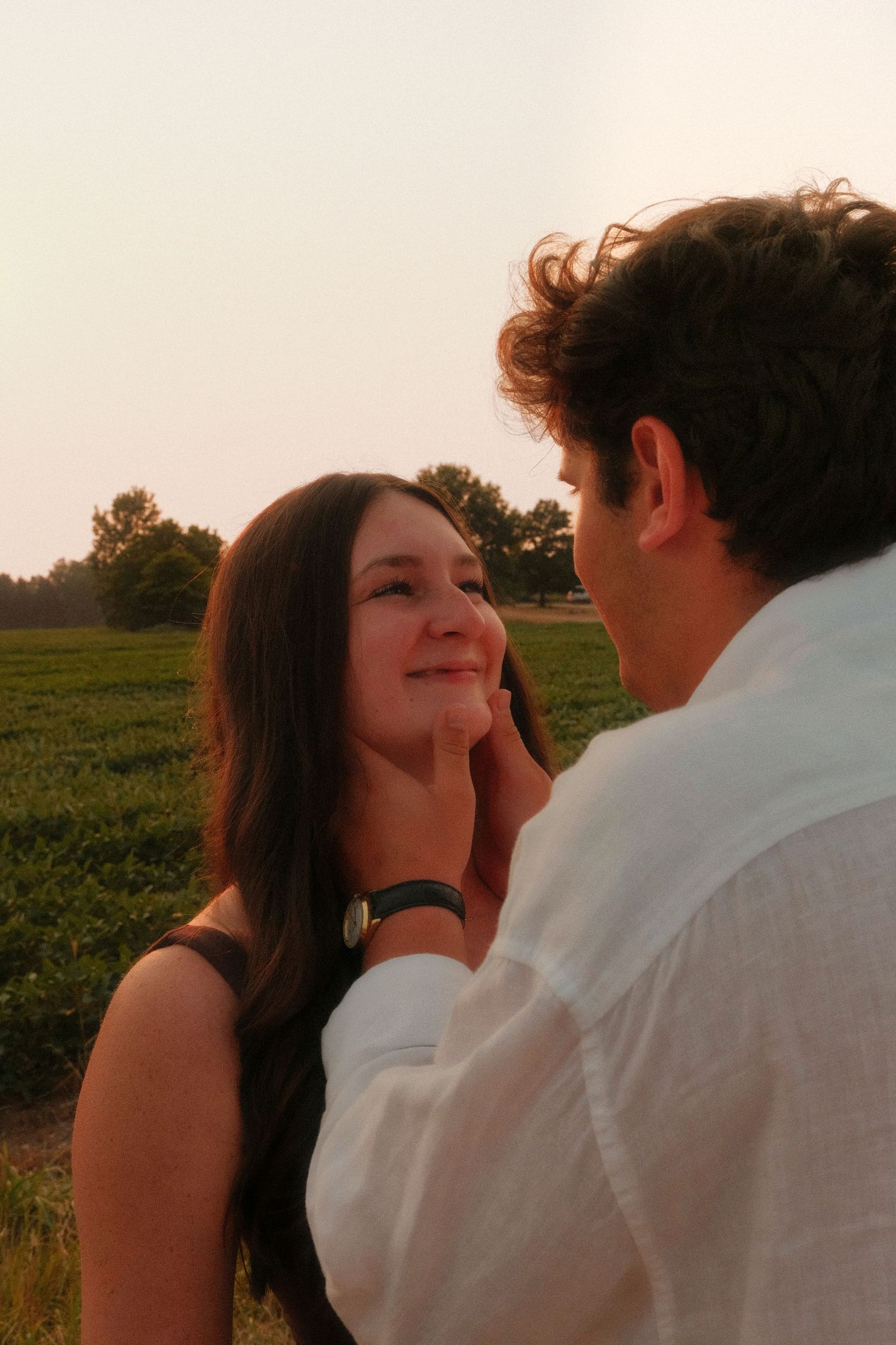 Man tenderly touching smiling woman's face in a golden hour field setting.