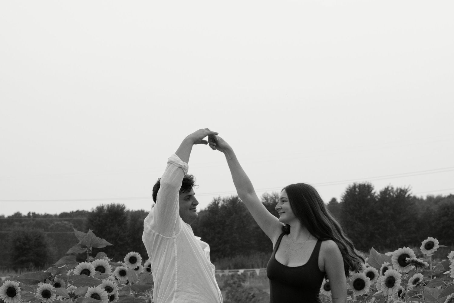 Black and white photo of couple dancing and holding hands up in a sunflower field.