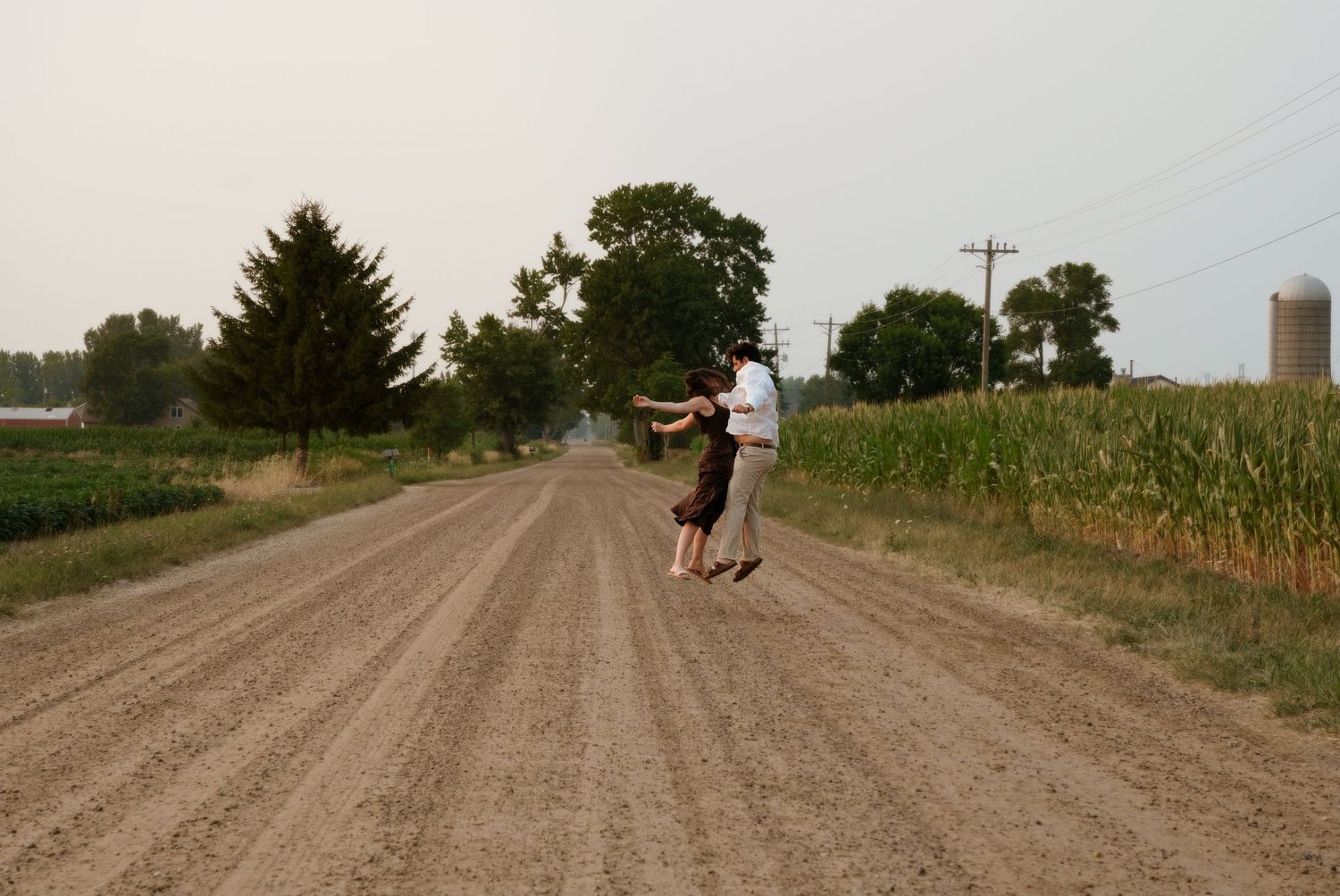 Couple dancing together on a wide rural dirt road surrounded by cornfields on a hazy day.