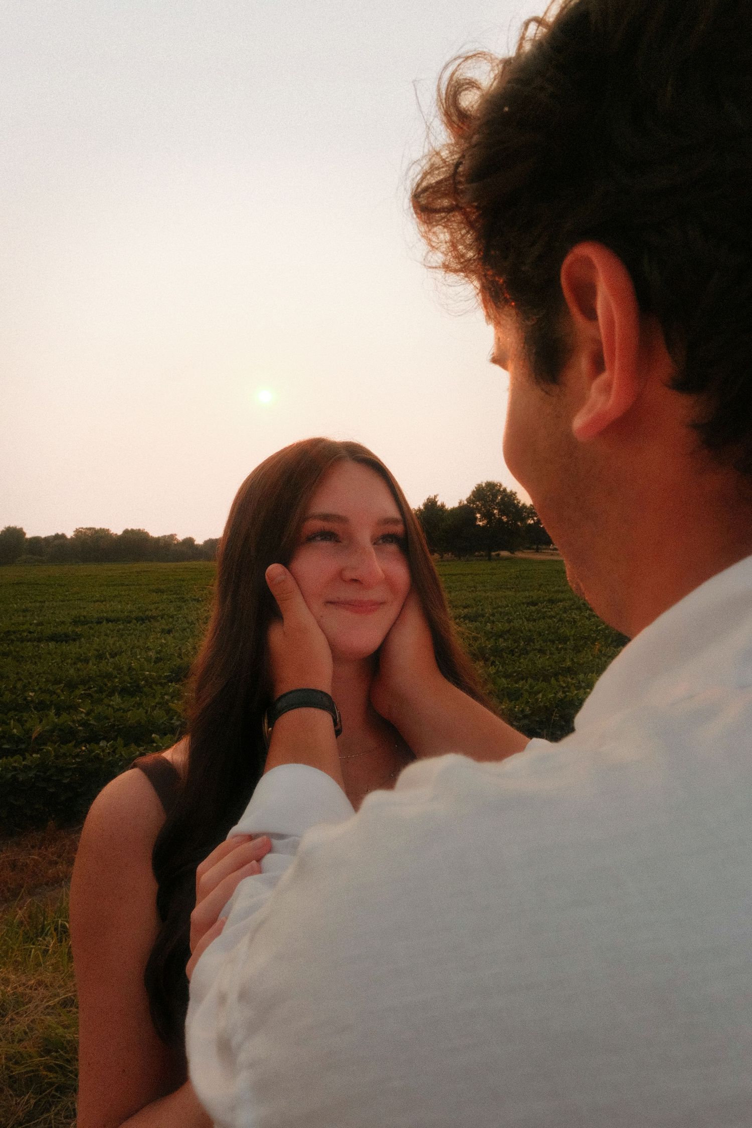 Man tenderly cupping womans face in sunflower field during romantic sunset photo session.