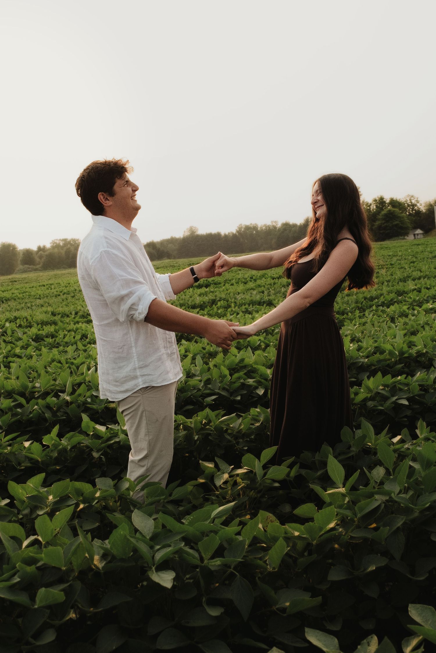 Joyful couple holding hands and spinning together in a green field at sunset.