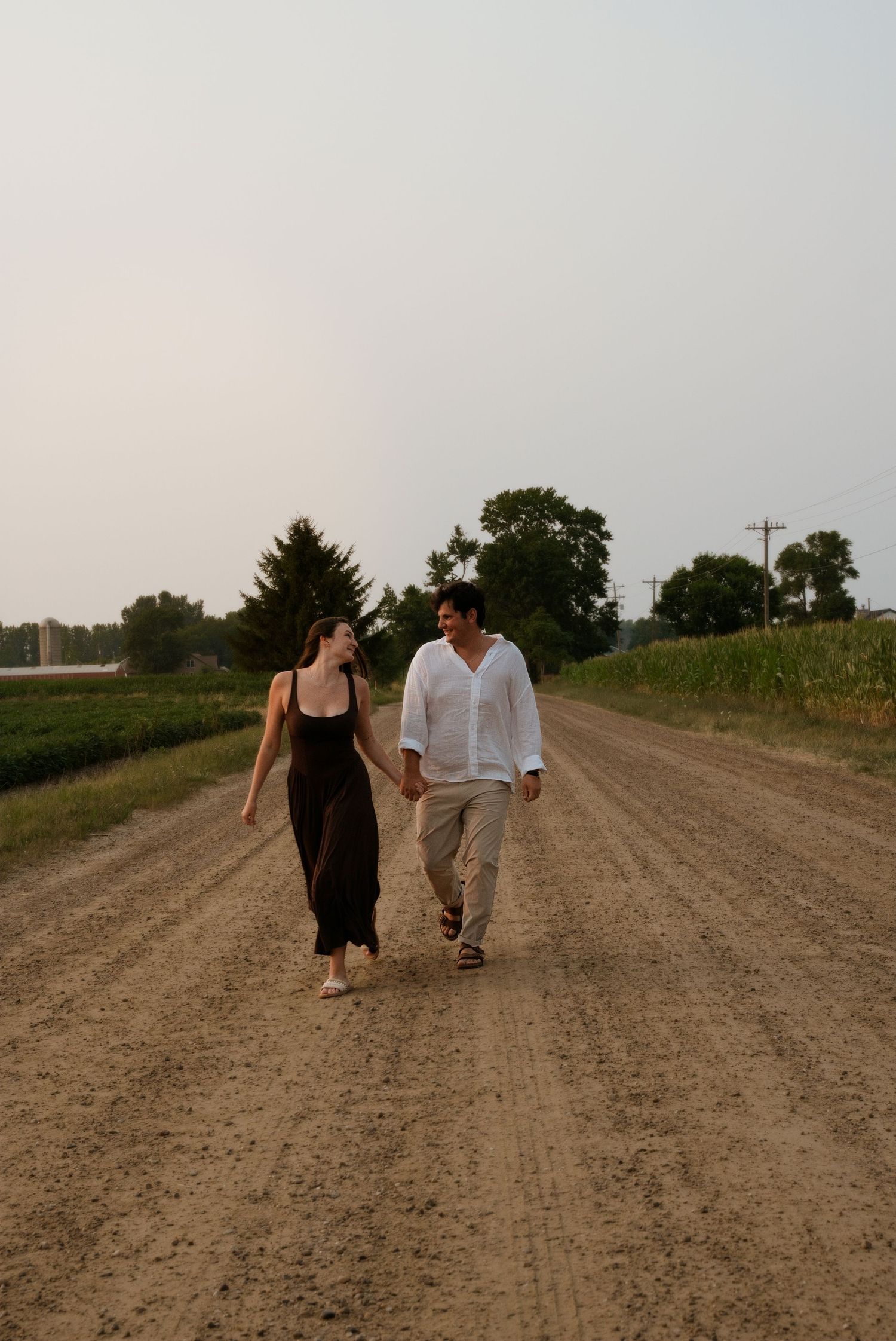 Happy couple walking hand in hand along a scenic dirt country road at sunset.