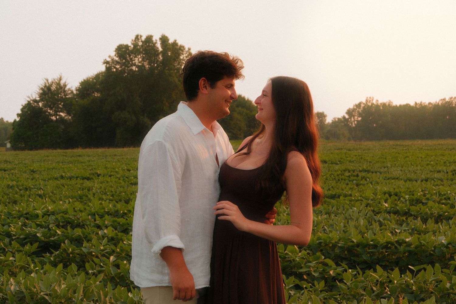 Couple sharing a romantic moment smiling at each other in a lush green field at golden hour.