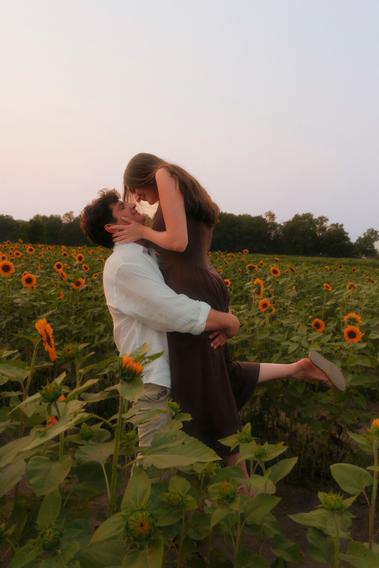Man lifting and kissing woman in a vibrant sunflower field at twilight.