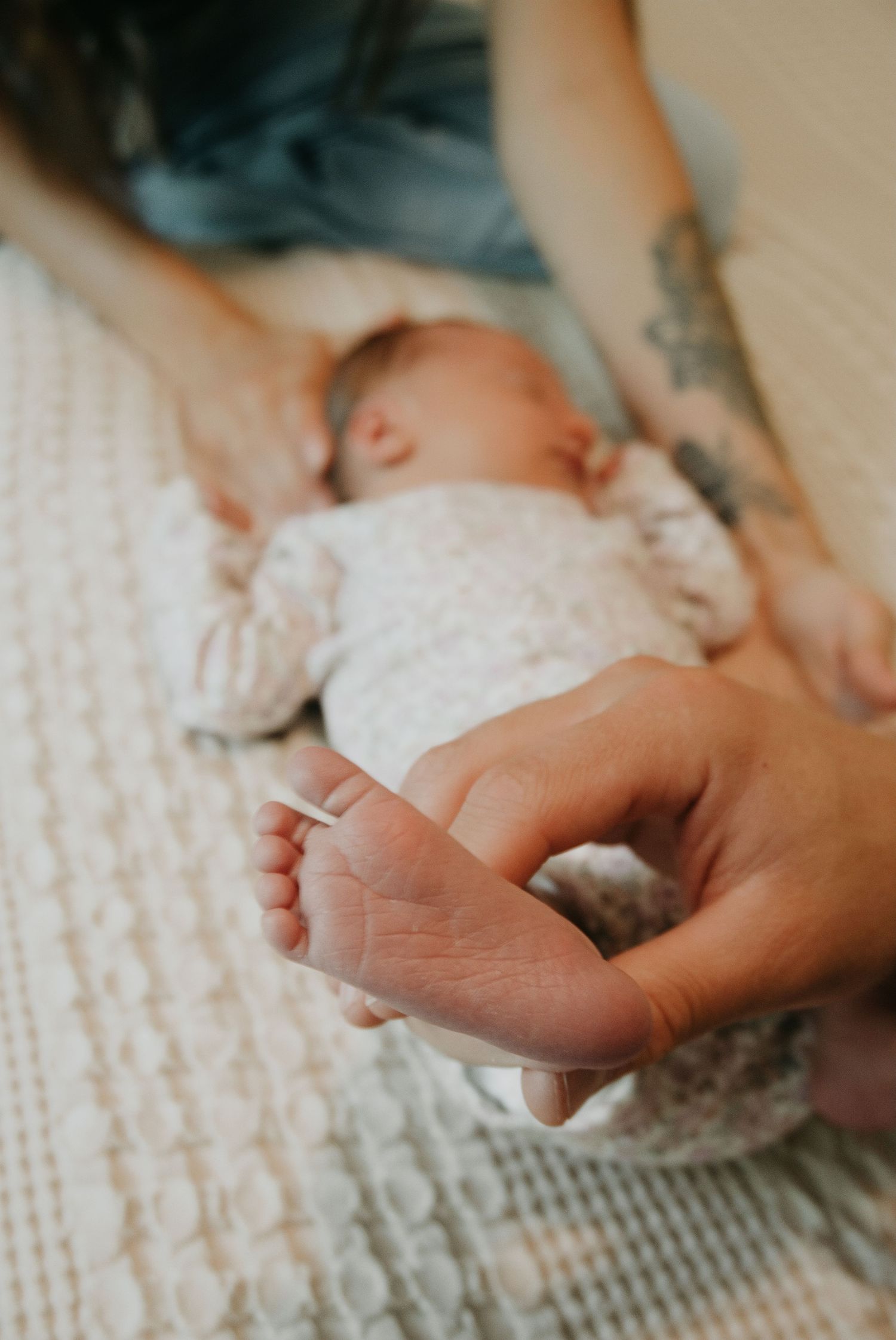 Close-up of adult hands gently holding a sleeping newborn baby's tiny feet on a soft white knit blanket.