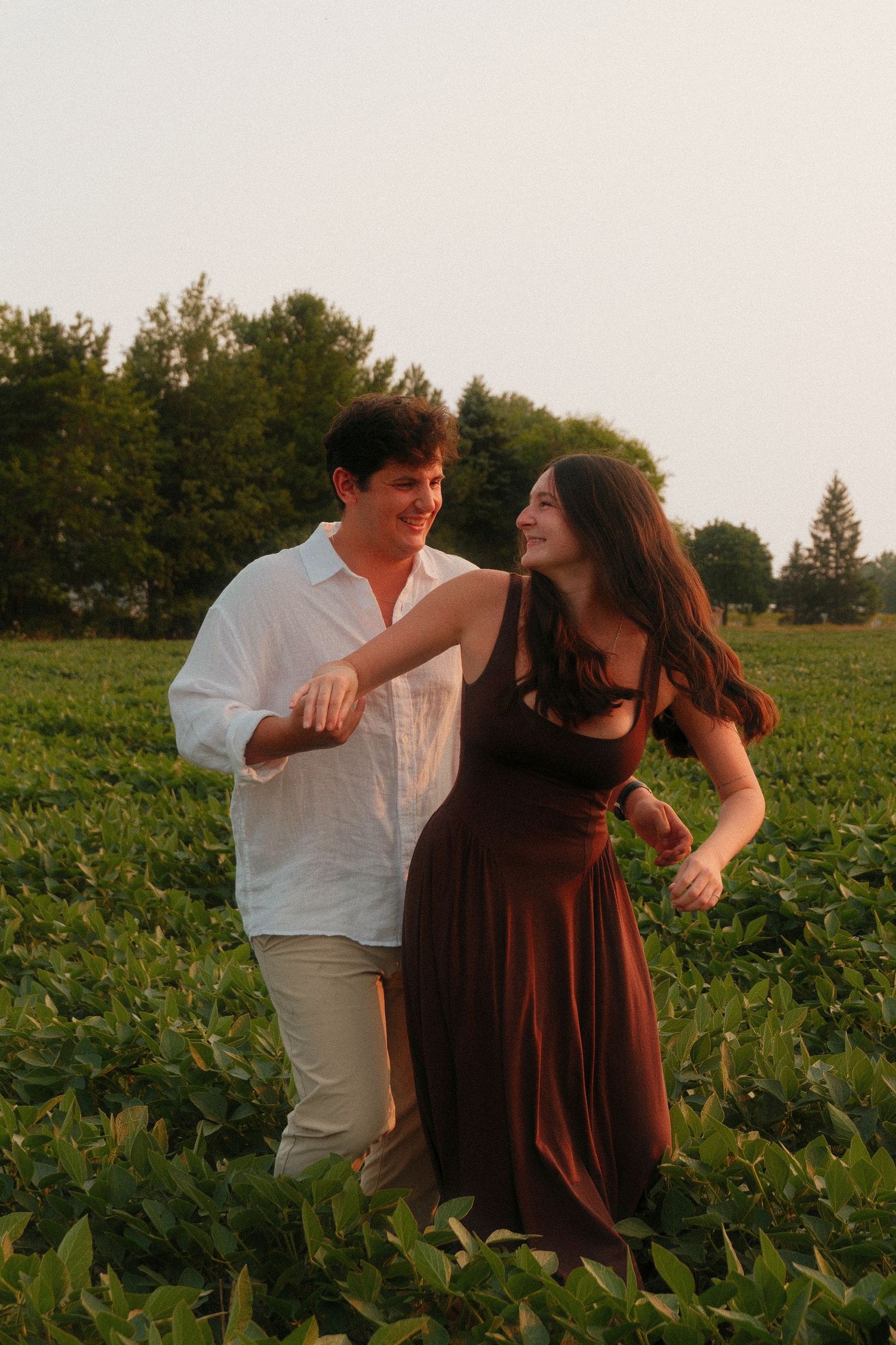 Happy couple walking and laughing together through a green farm field at sunset.