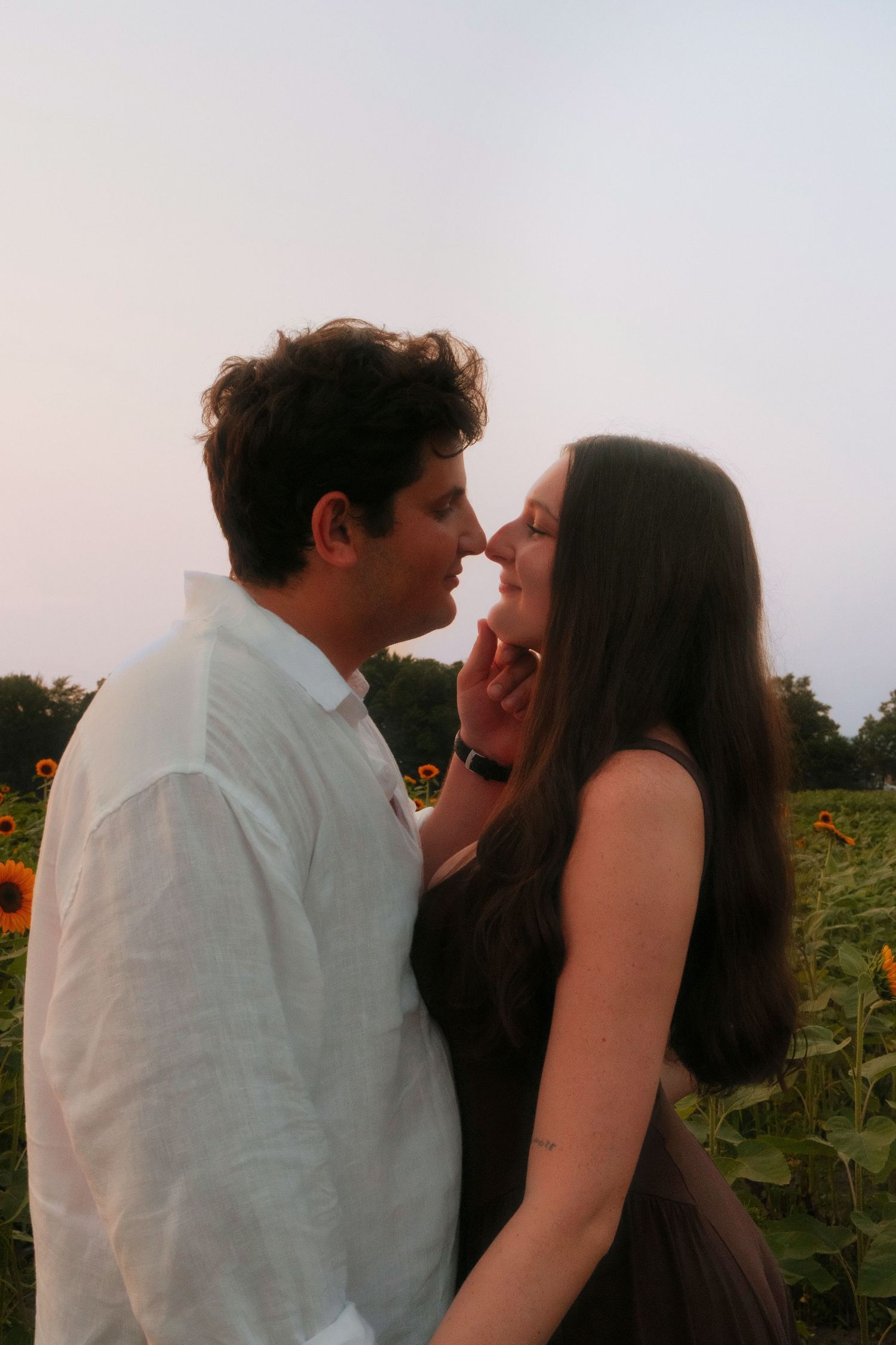 Young couple sharing an intimate moment, nearly kissing, with sunflowers blooming in the background.