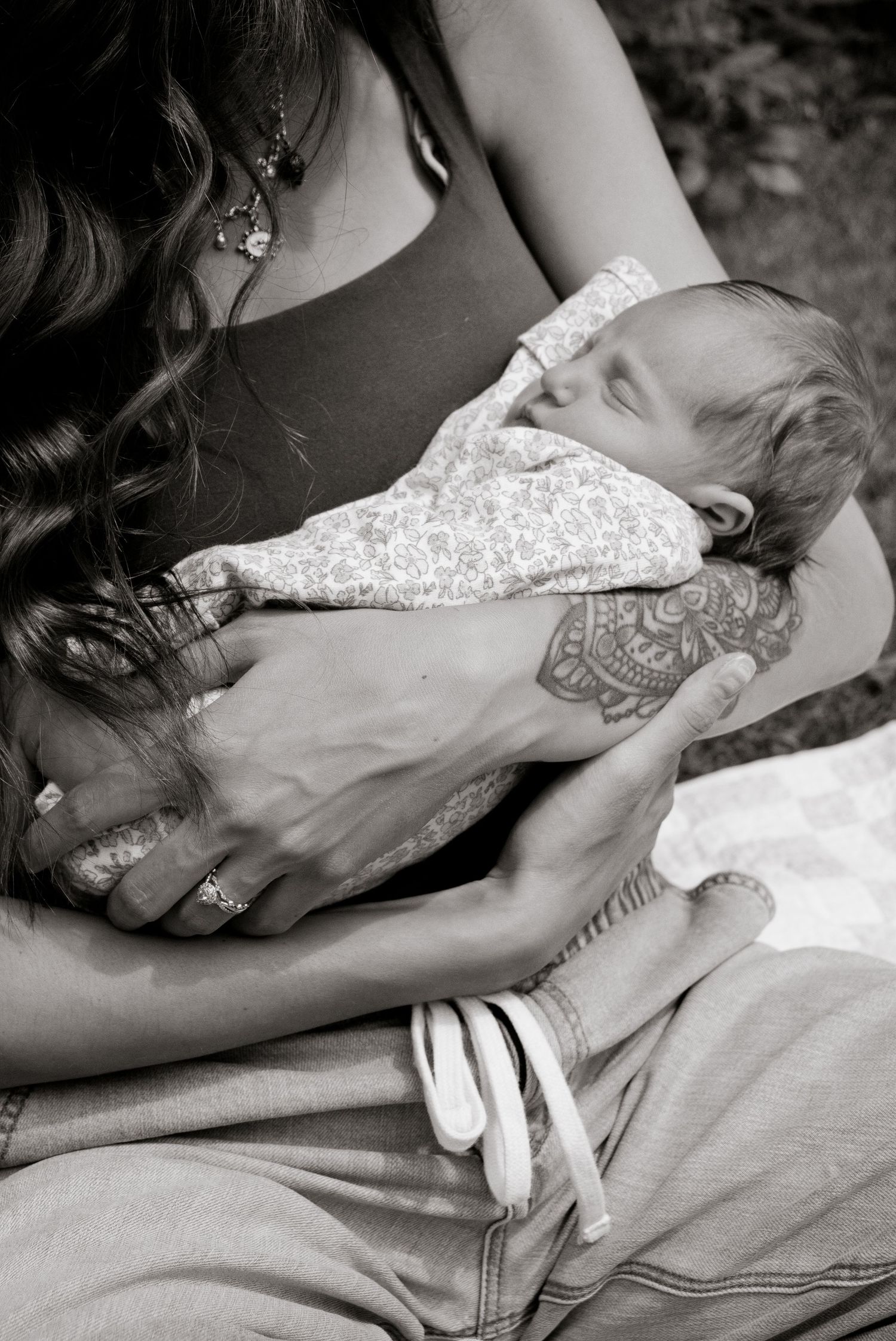 Black and white photo of a mother cradling her sleeping newborn baby, with henna tattoo on her hand.