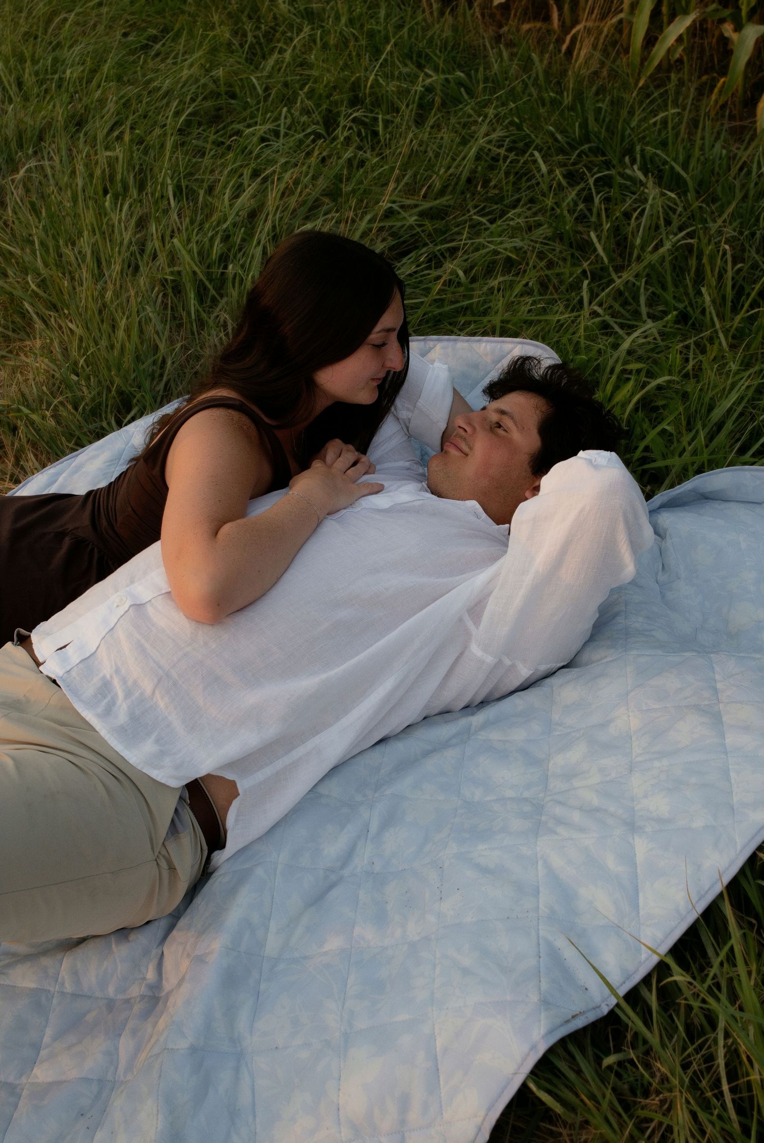 Couple lying on a blanket in tall grass sharing a romantic intimate moment.