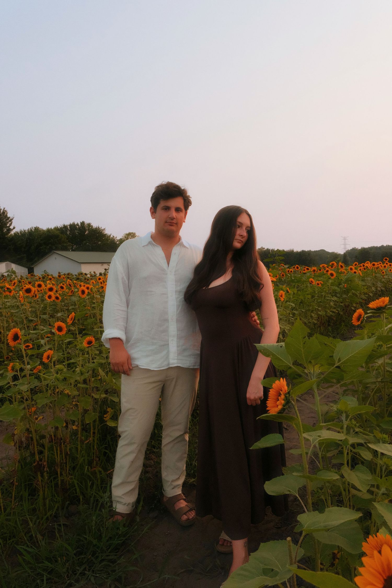 Young couple posing together in a vibrant sunflower field during golden hour at dusk.