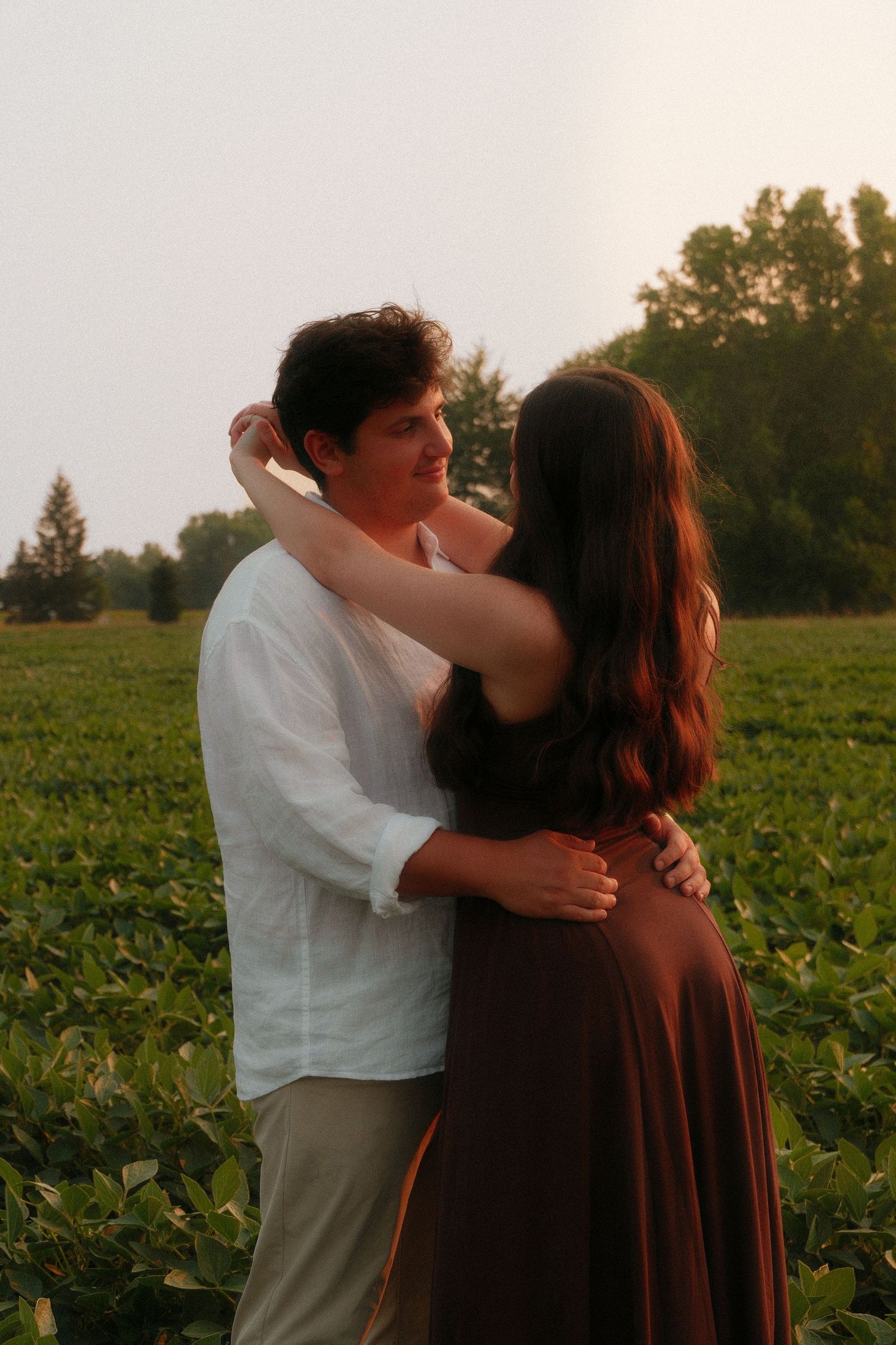 Romantic couple embracing and gazing at each other in a scenic green field.