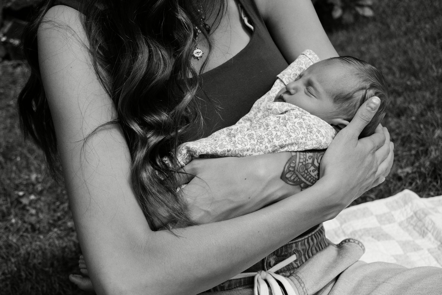 Black and white photo of a mother tenderly cradling her newborn baby outdoors on grass.