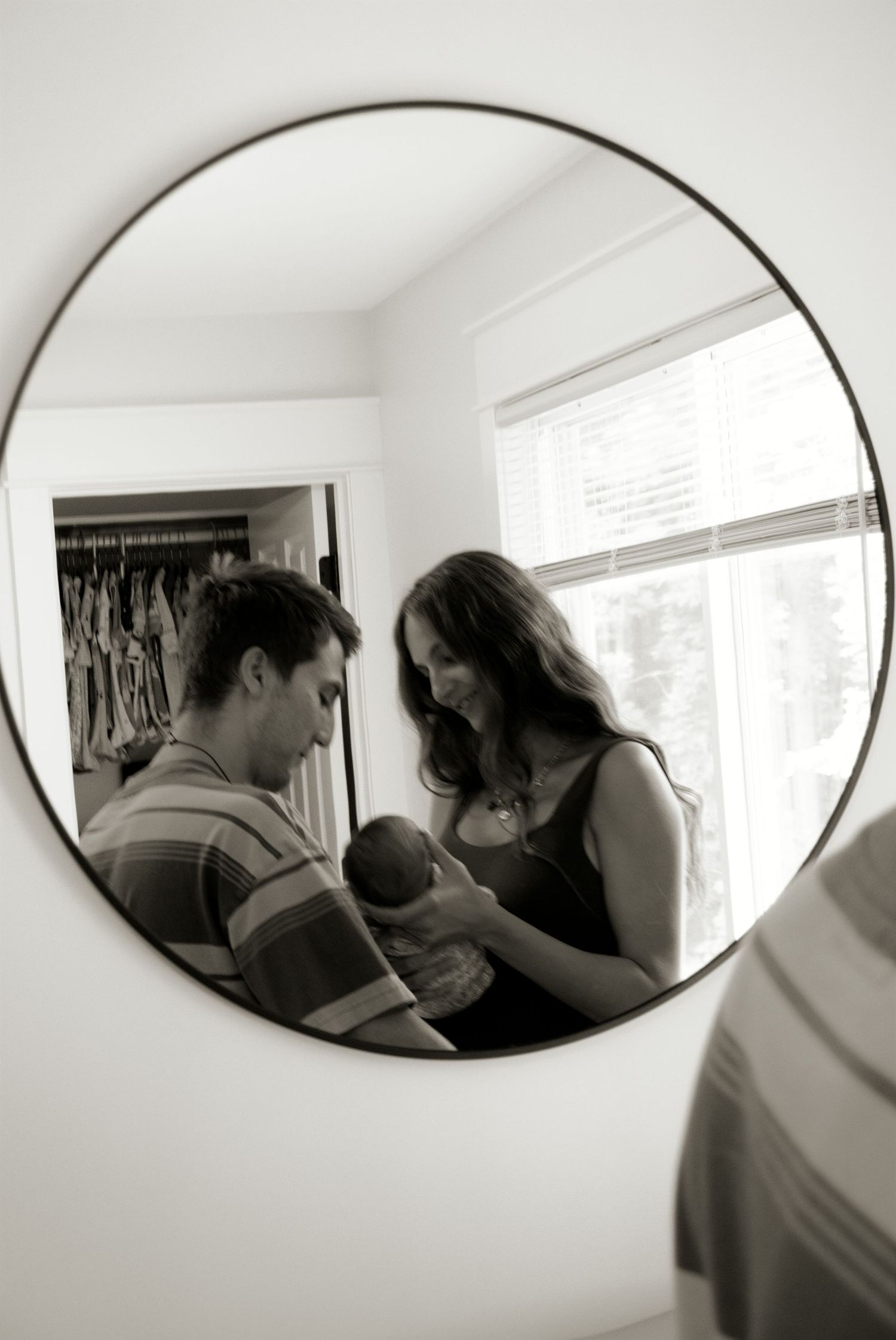 New parents admiring their newborn baby reflected in a round bedroom mirror.