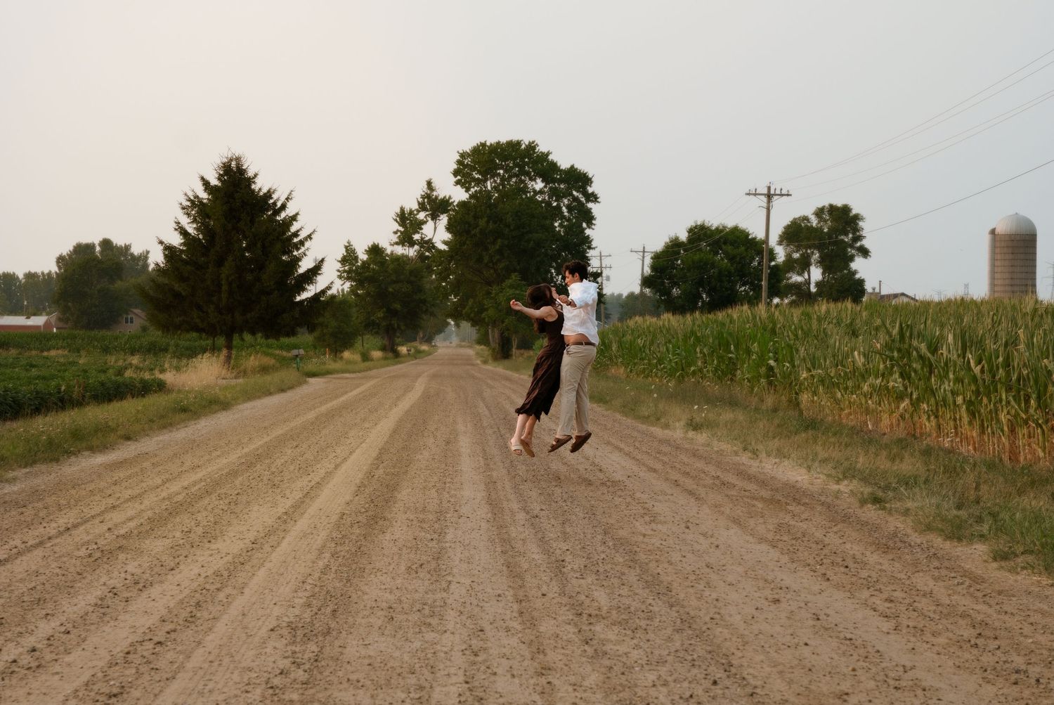 Couple spinning joyfully on a scenic country dirt road beside tall cornfields at dusk.