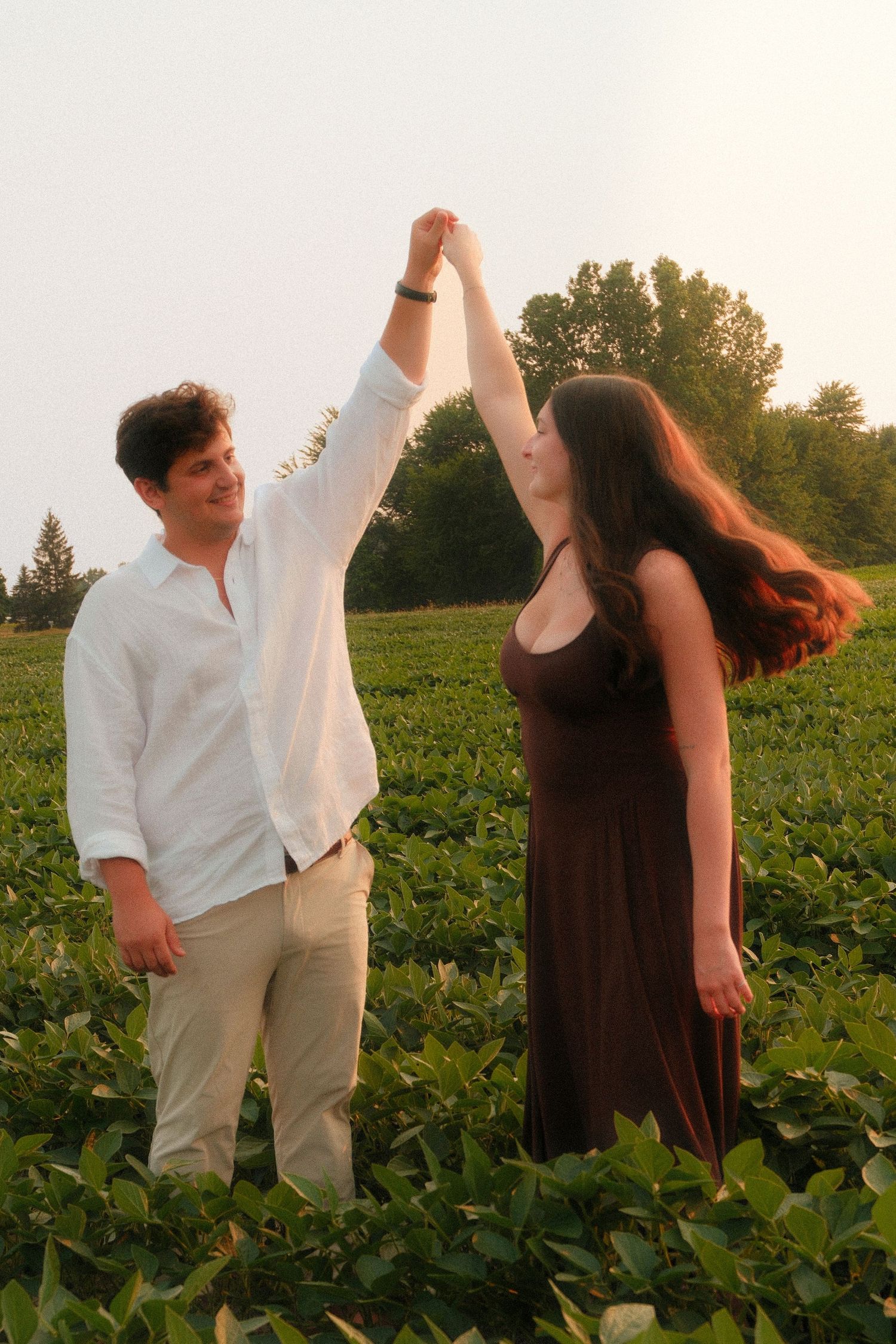 Happy couple dancing together in a green field, man spinning woman at sunset.