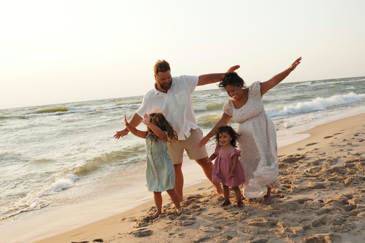 Family of four joyfully playing on a sandy beach near ocean waves on a sunny day.