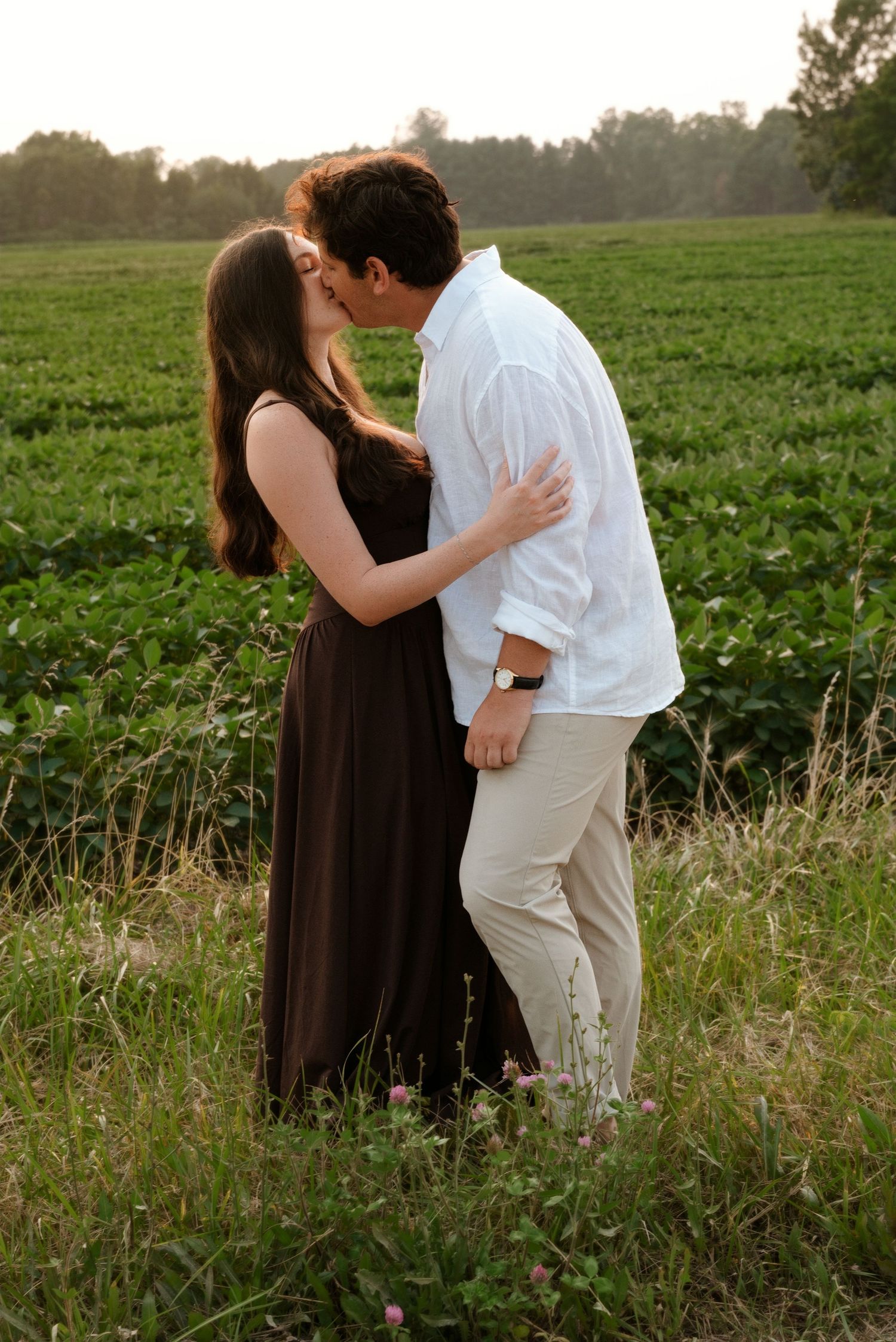 Couple sharing a romantic kiss in a lush green field during golden hour.