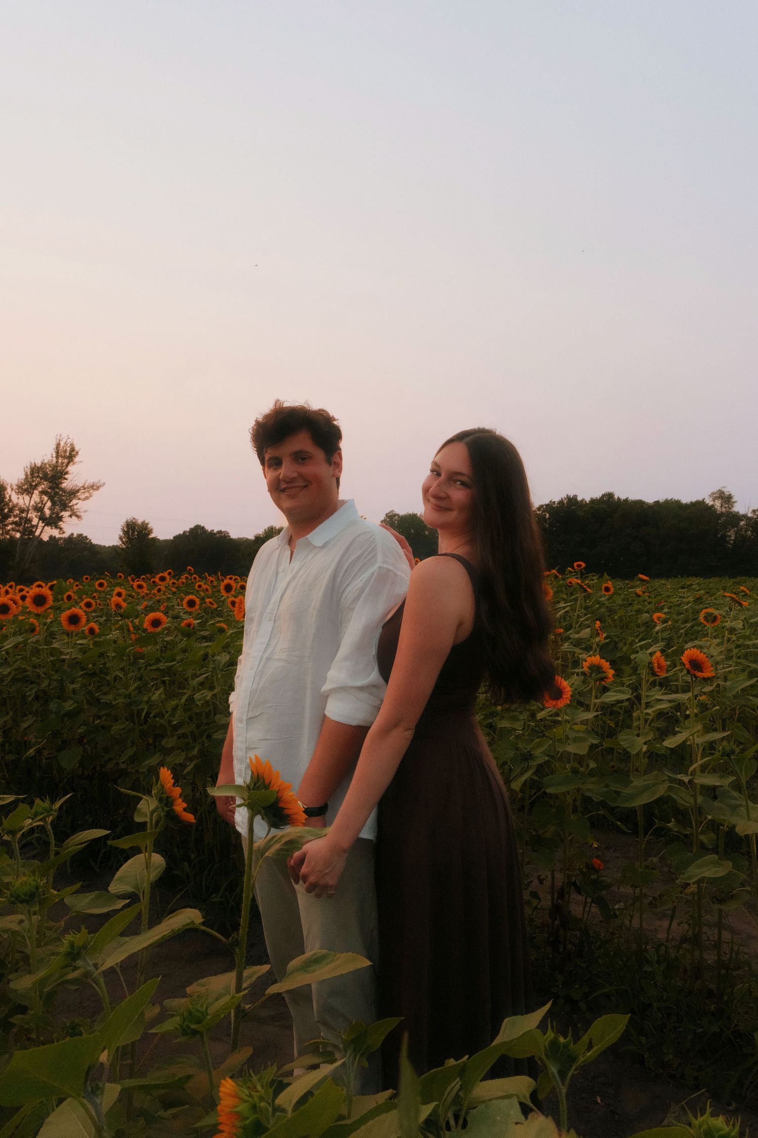 Smiling couple posing together in golden sunflower field during romantic outdoor photo shoot.