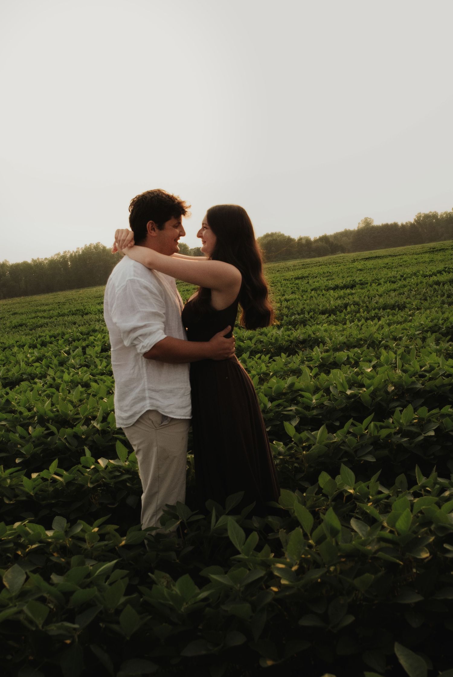 Couple embracing and smiling at each other in a lush green field at dusk.