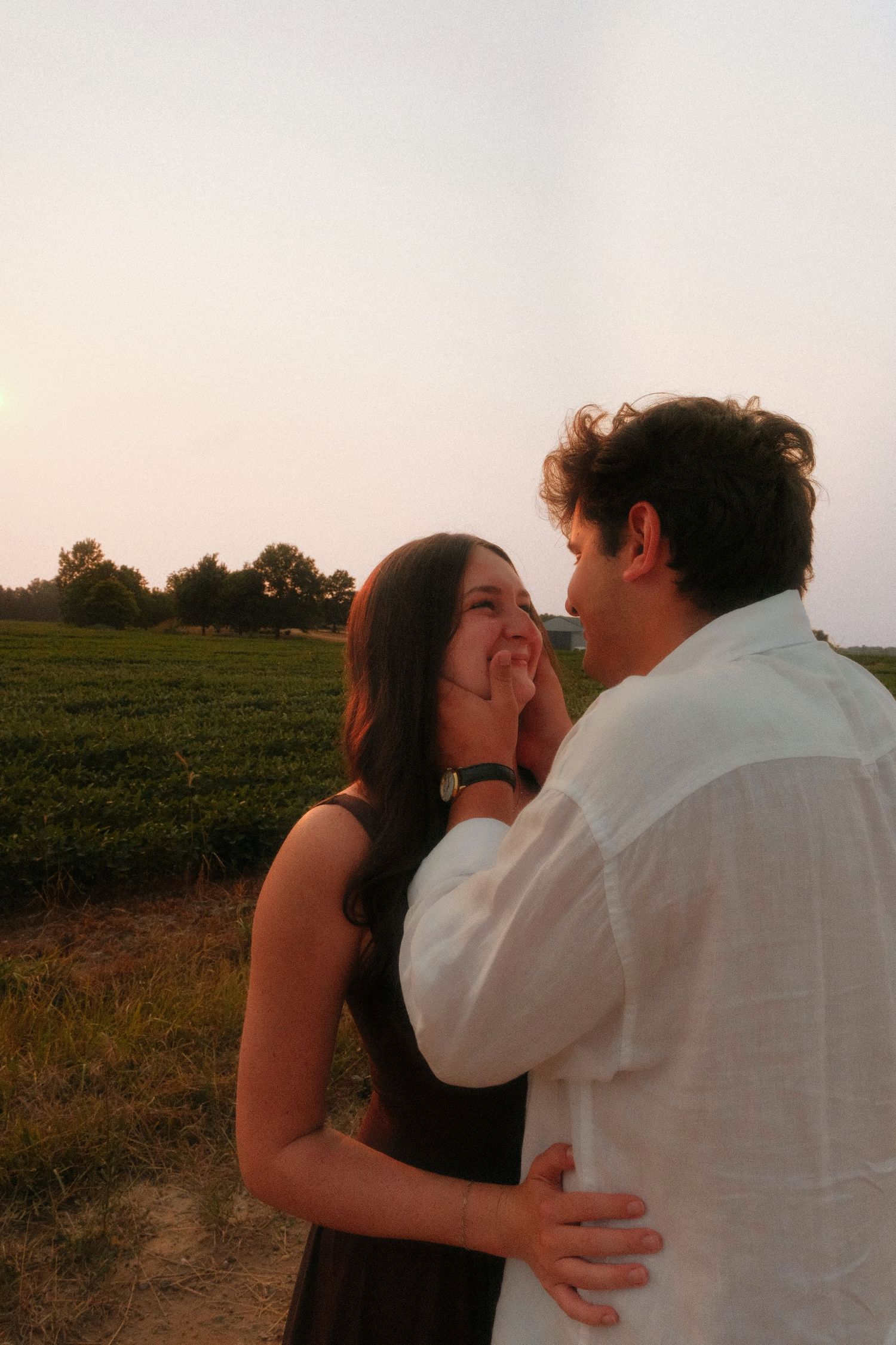 A loving couple shares an intimate moment as the man gently cups the womans face in a field at dusk.