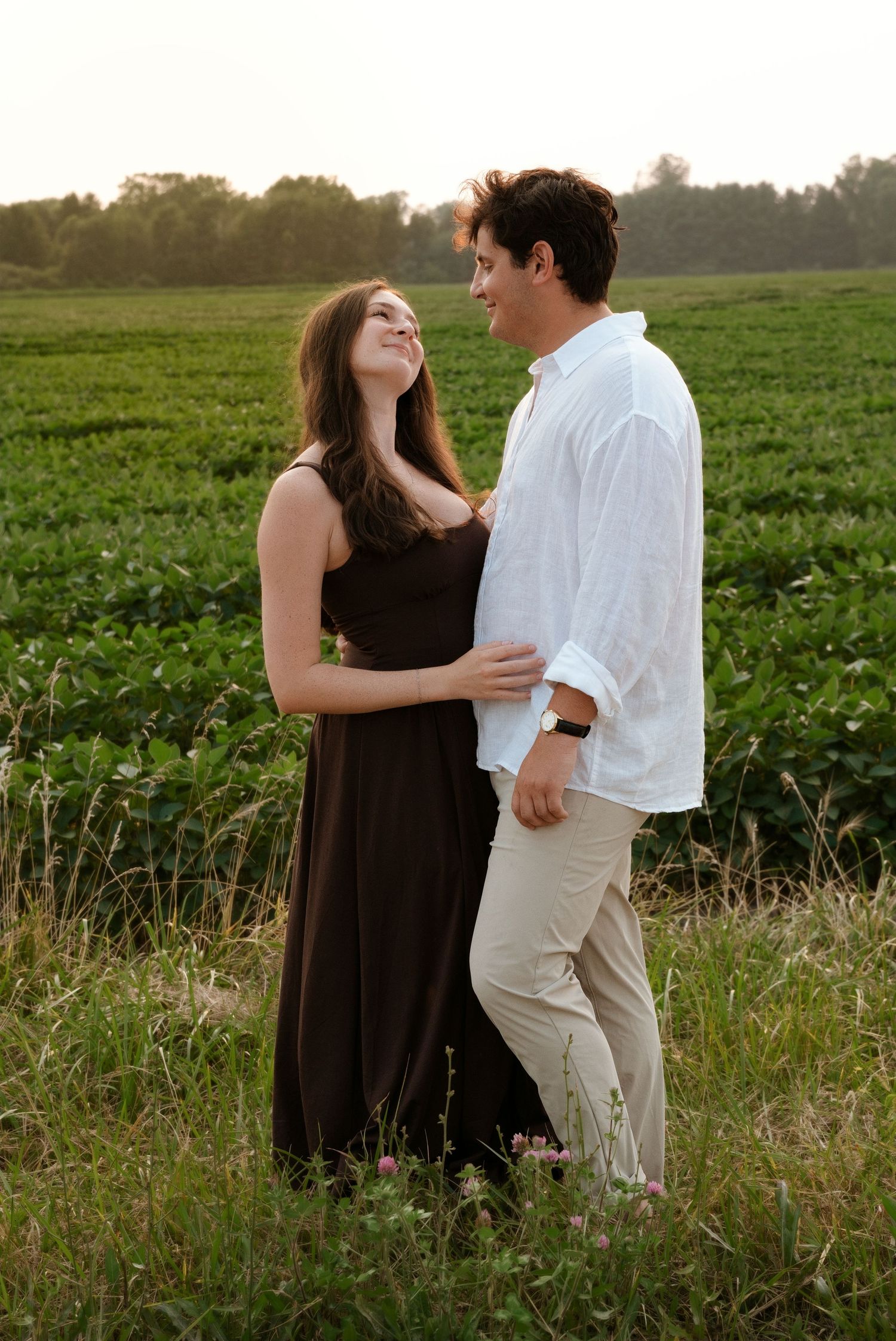 Happy couple laughing and embracing in a lush green field during golden hour sunset lighting.