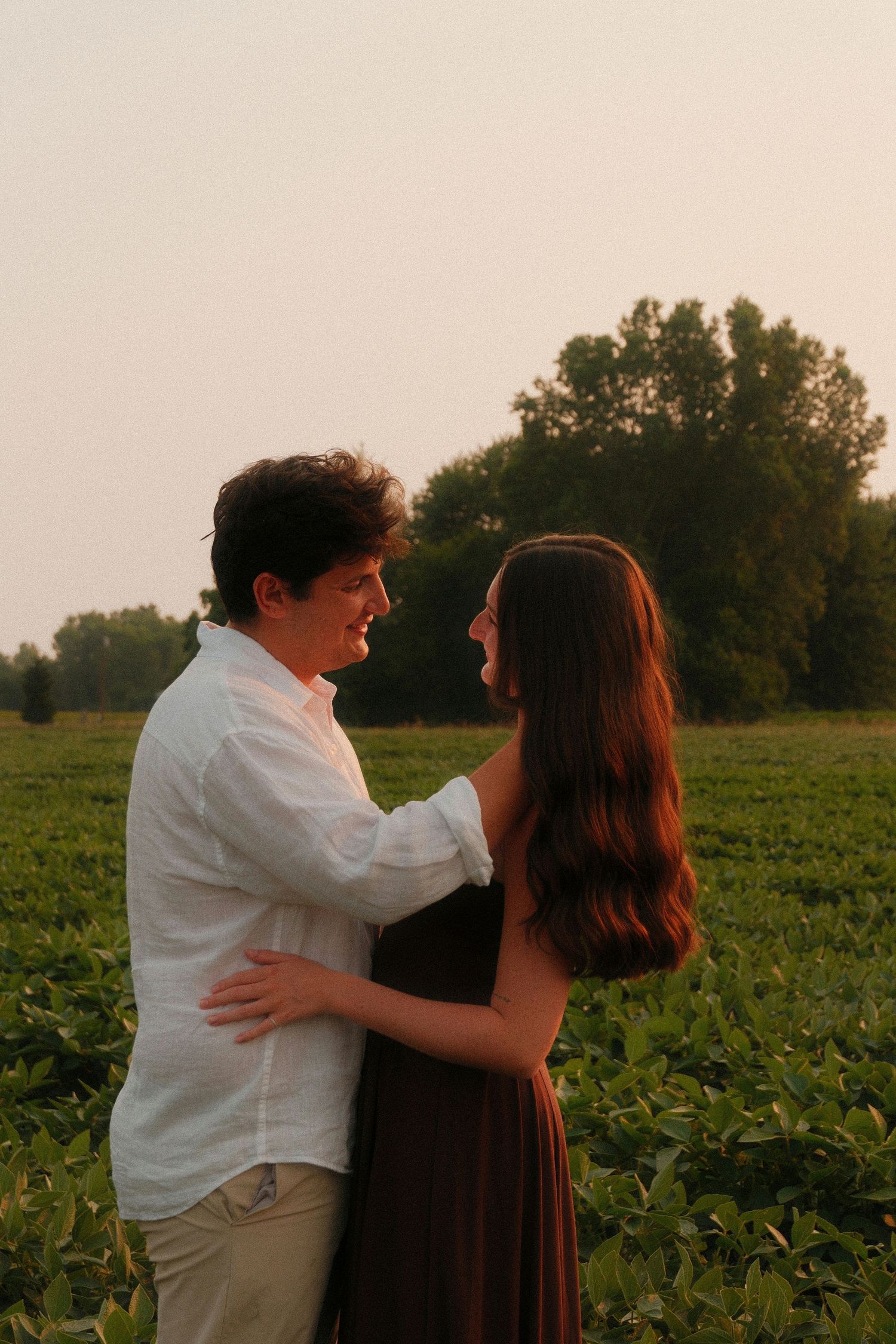 Young couple embracing in a lush green field at golden hour sunset.